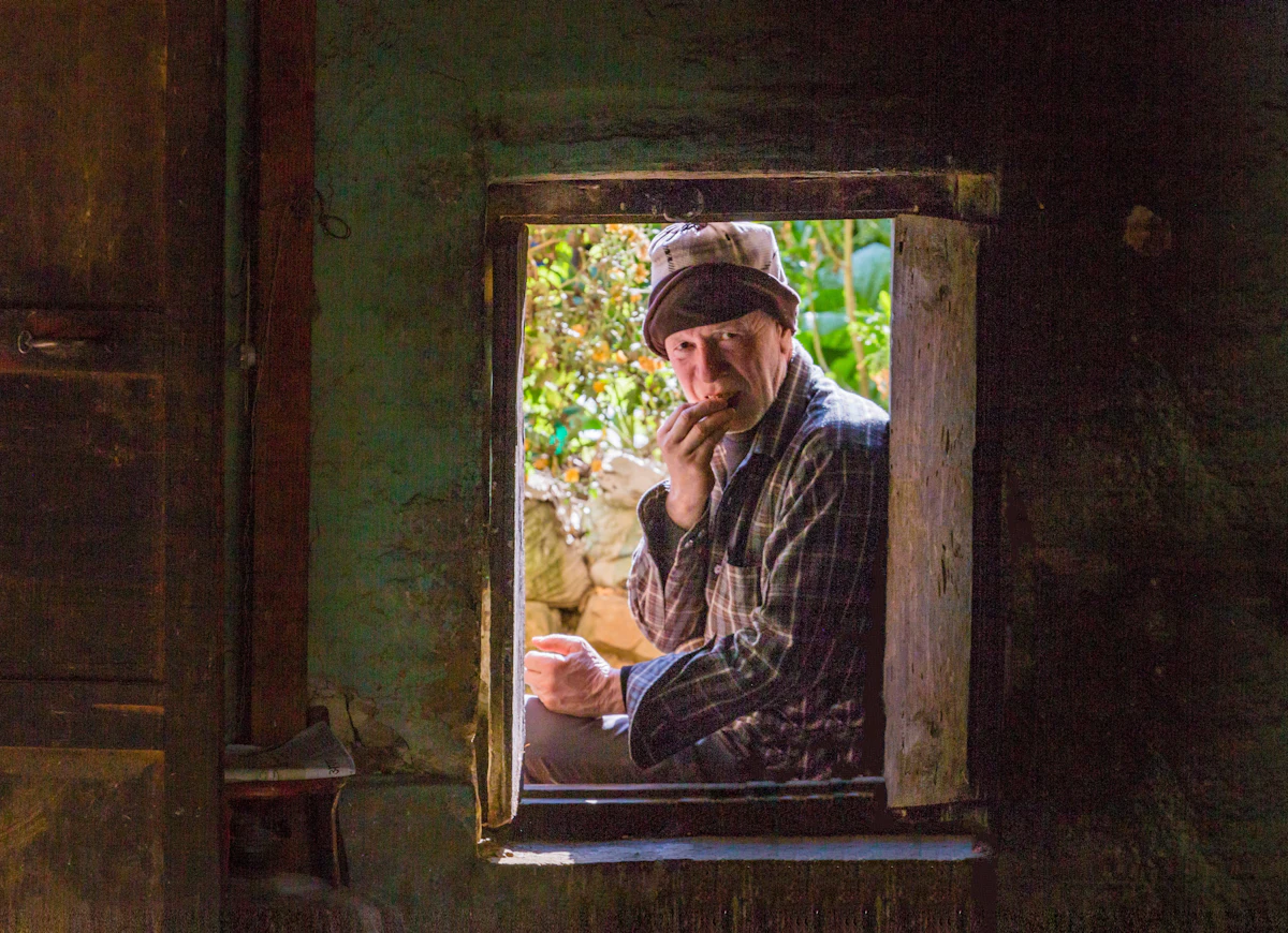 An older man sits quietly beside a window, looking out in a contemplative moment