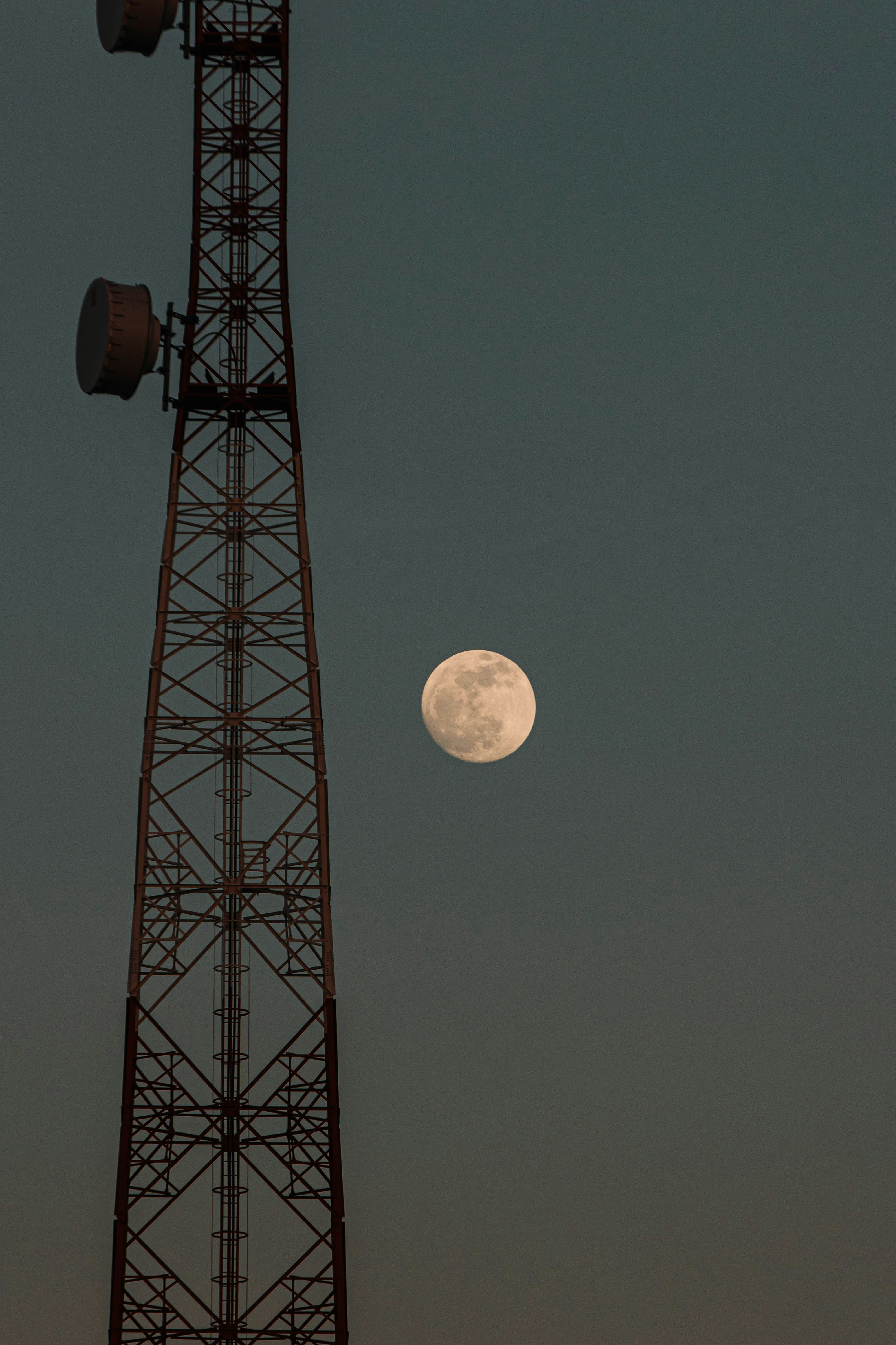 A full moon hangs near a tall cell tower.