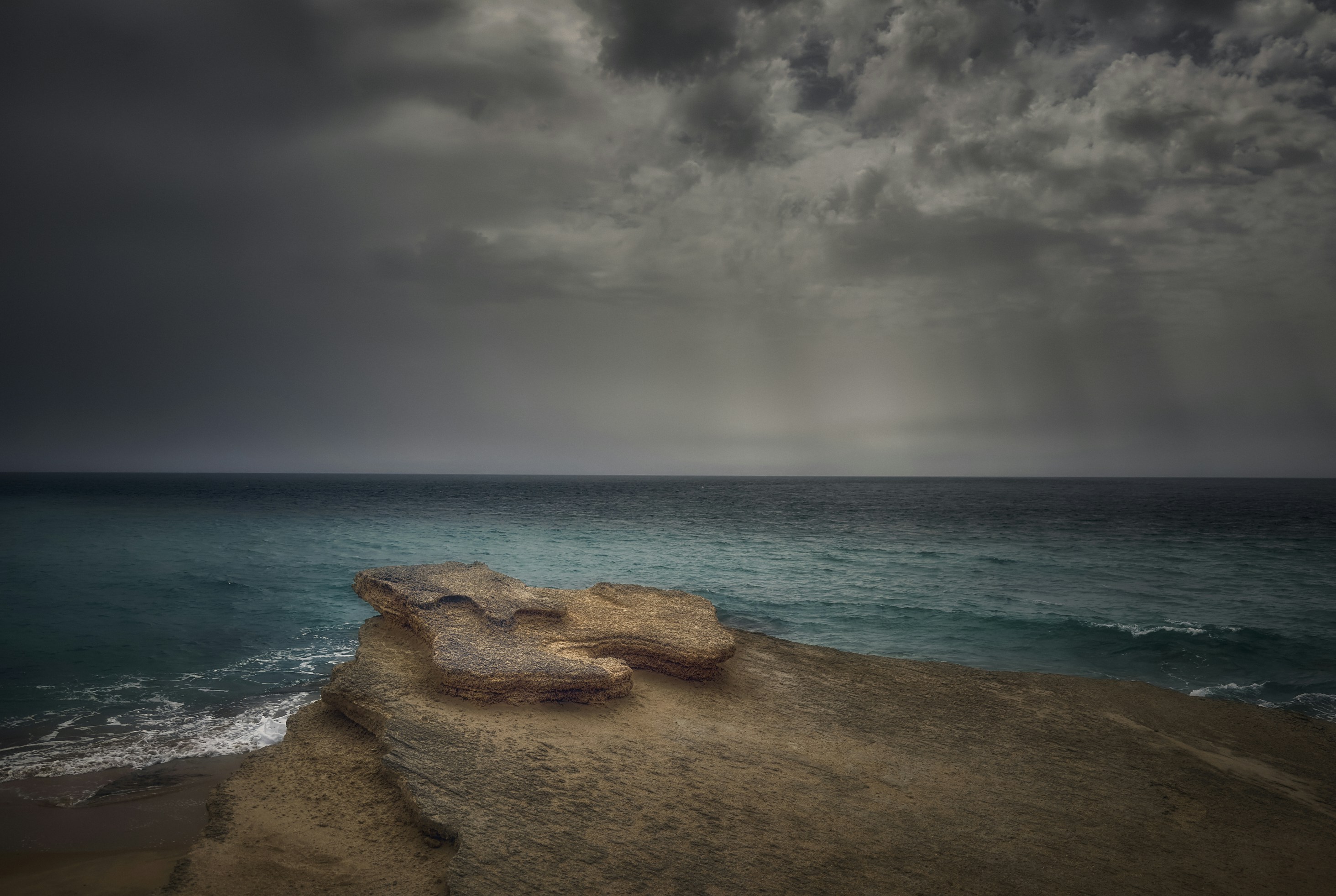 Rocky shore meets turquoise ocean under stormy clouds