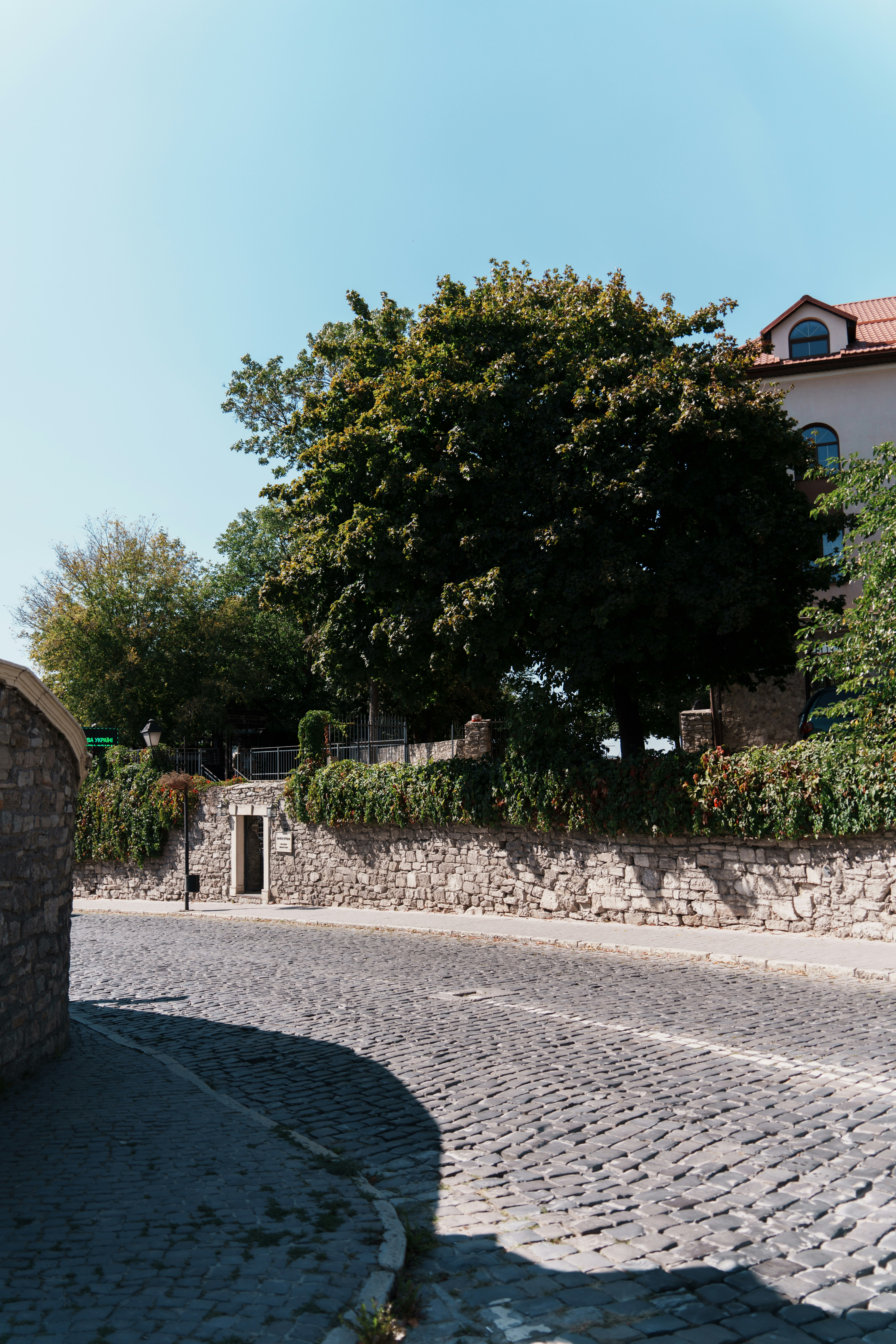 Cobblestone street leads to a stone wall and trees.