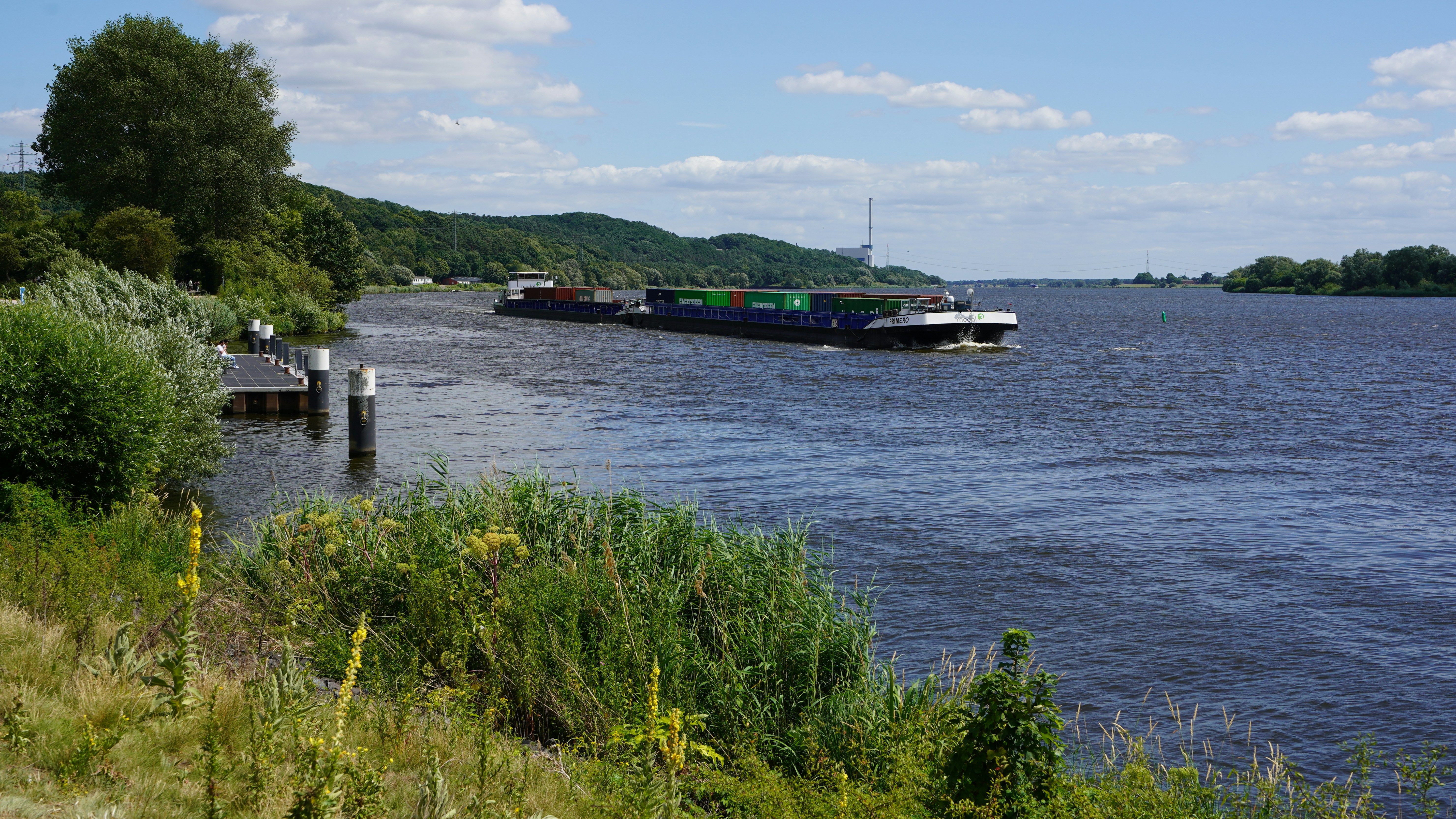 A barge travels down a wide river with green banks.