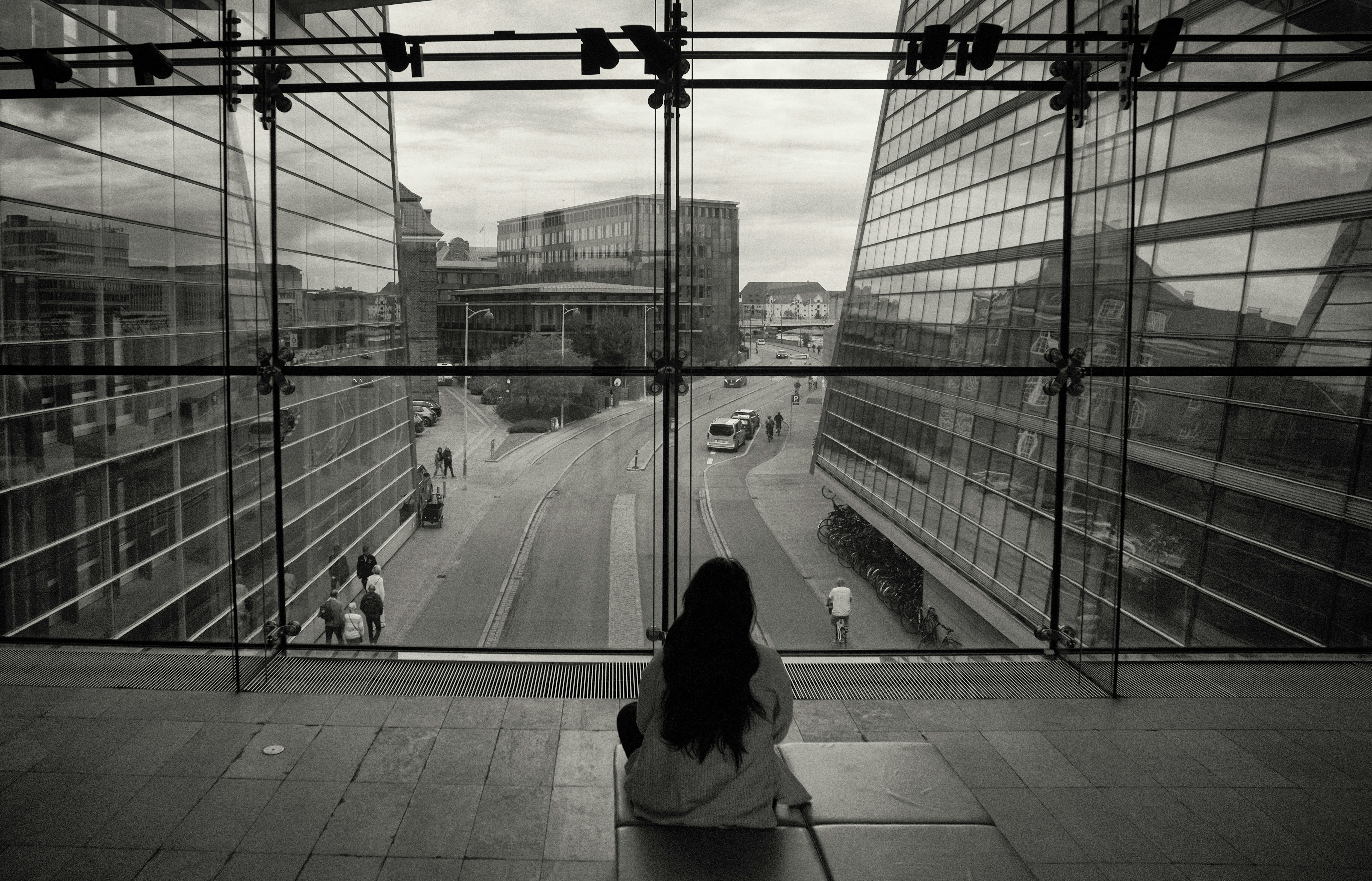 Woman looking out a large glass window at city street
