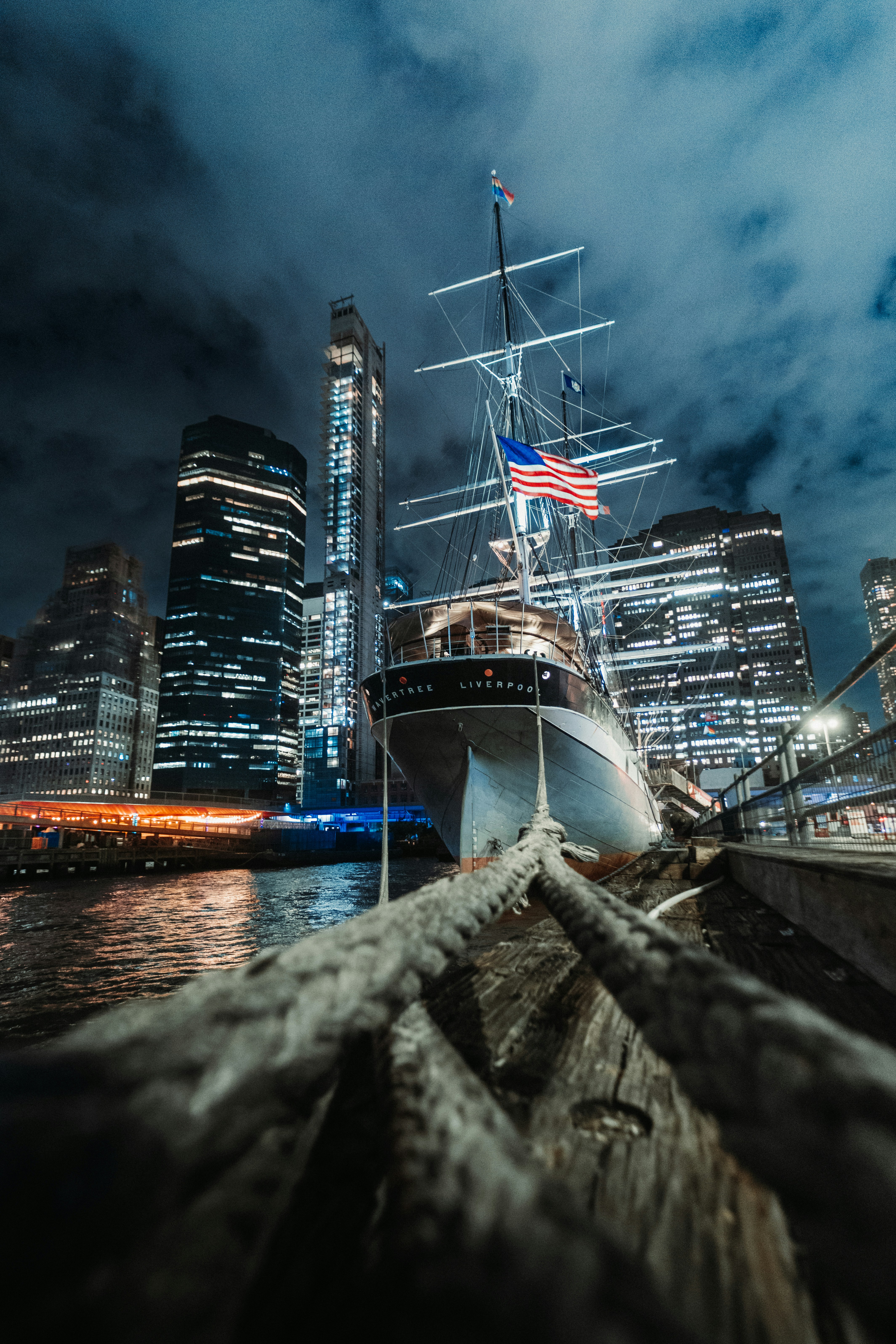 Historic ship docked by illuminated city skyline at night