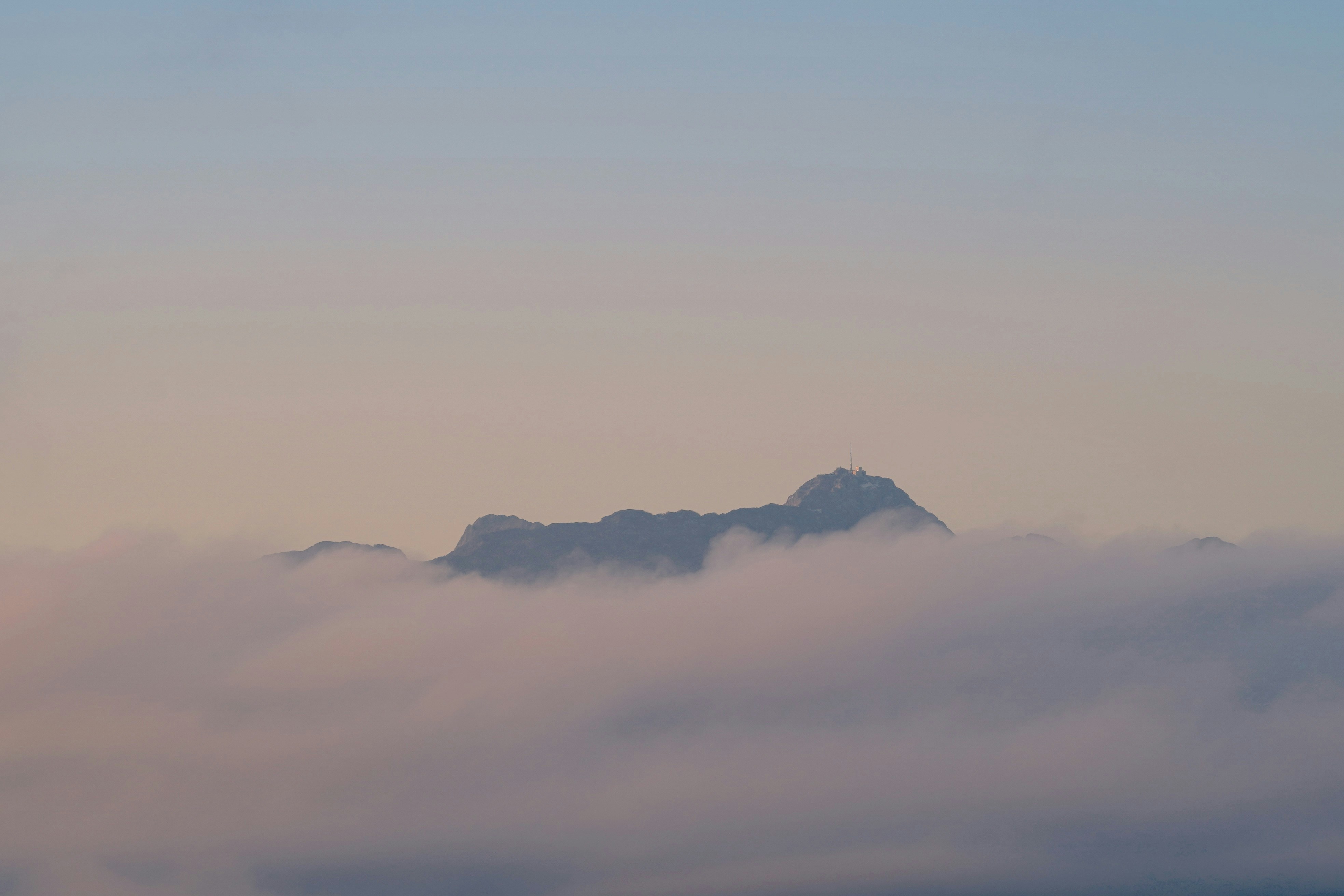 Mountain peak emerging from soft clouds at dawn.