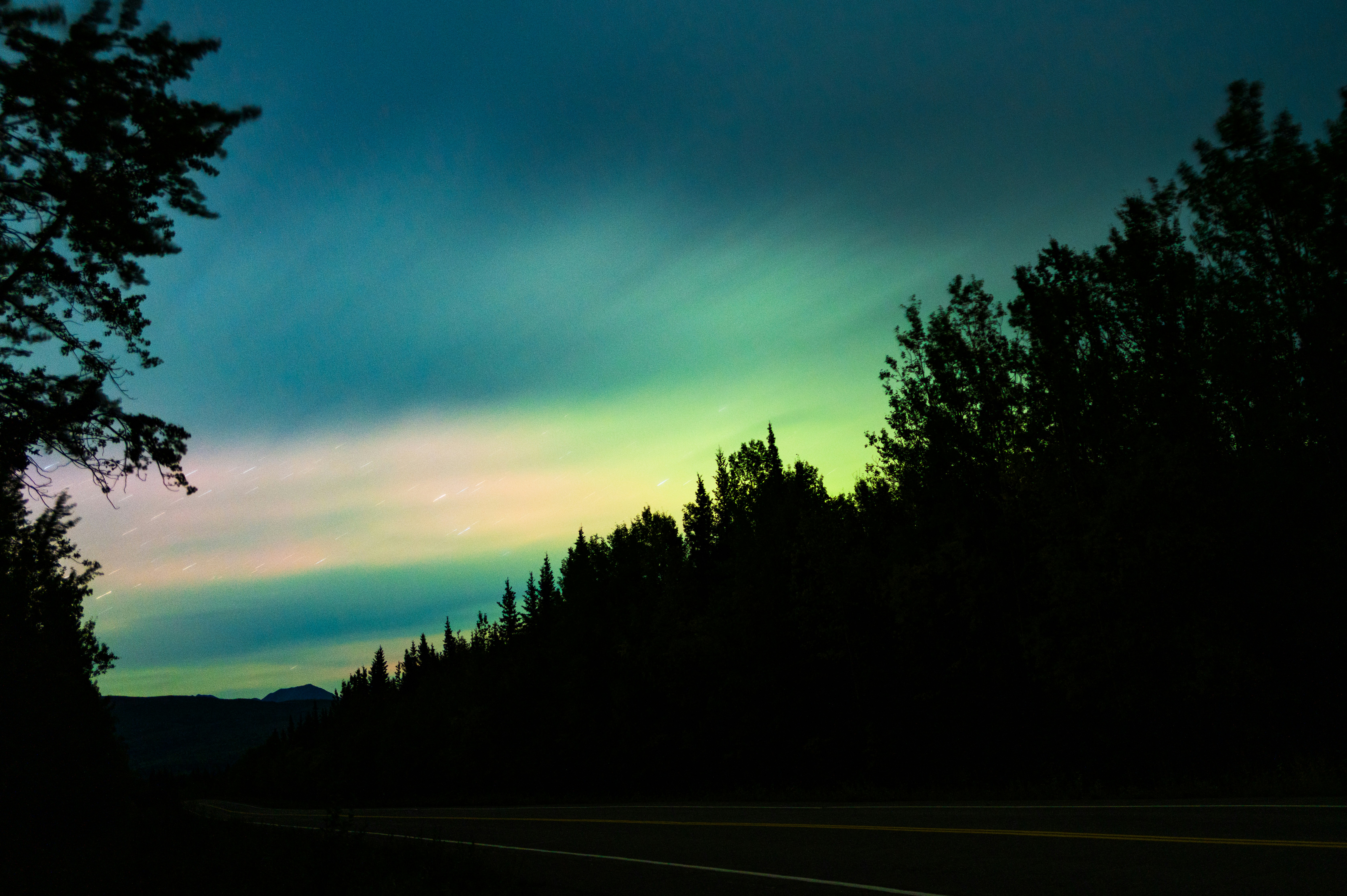 Colorful sky over a dark forest and road.
