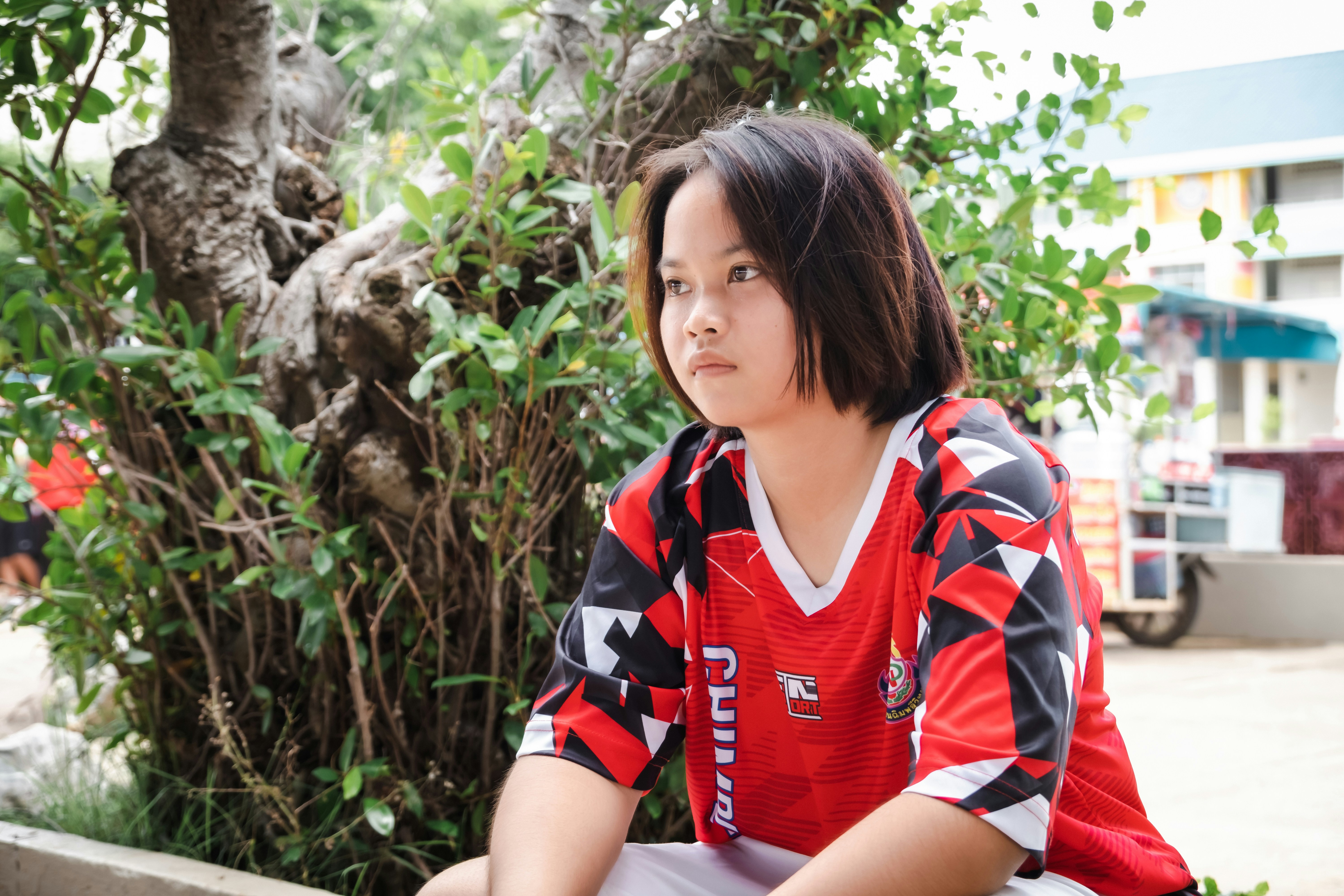A young girl in a red shirt looks away thoughtfully