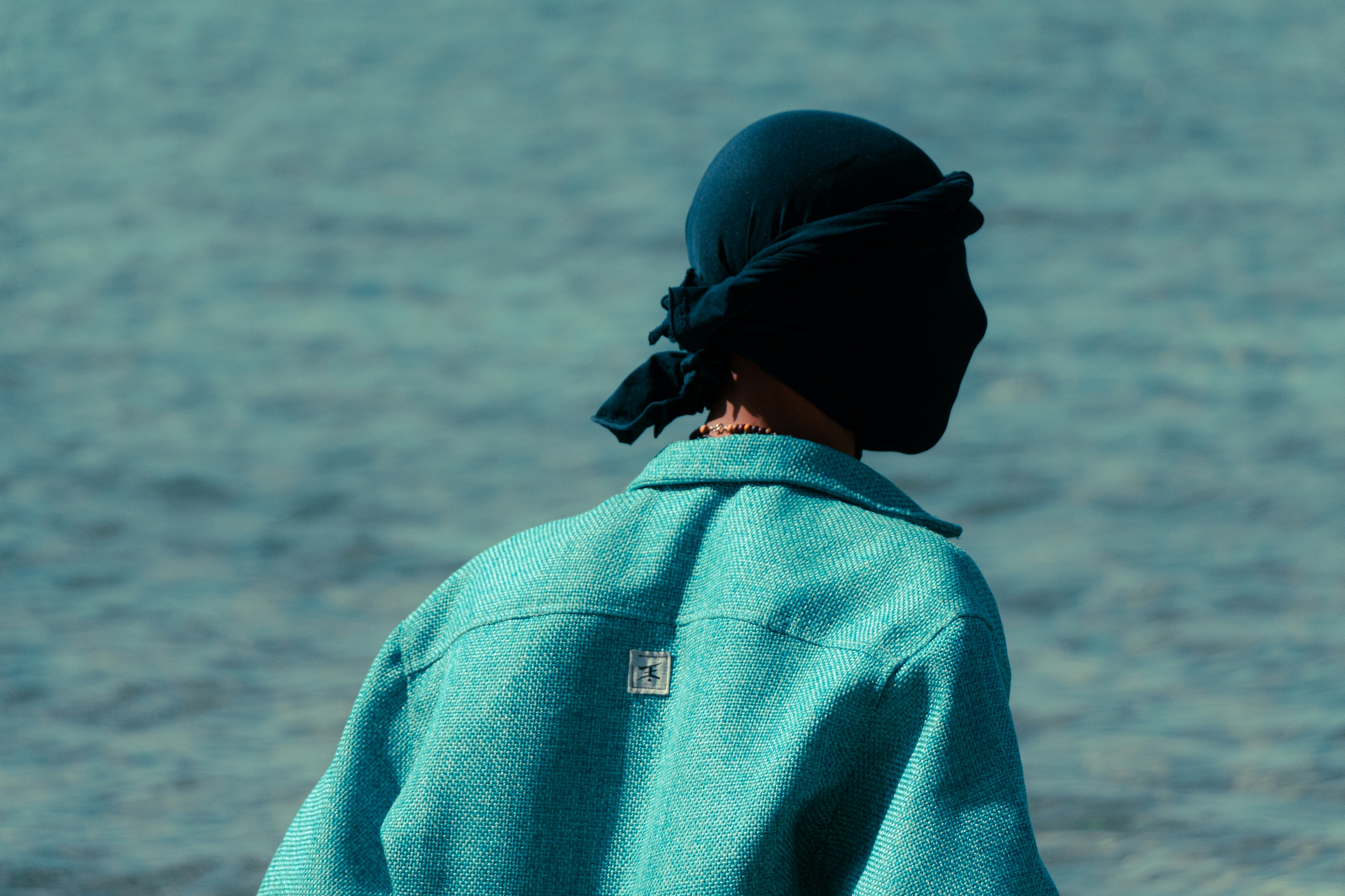 Person wearing a dark head covering and teal jacket.