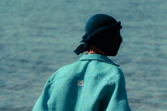 Person wearing a dark head covering and teal jacket.