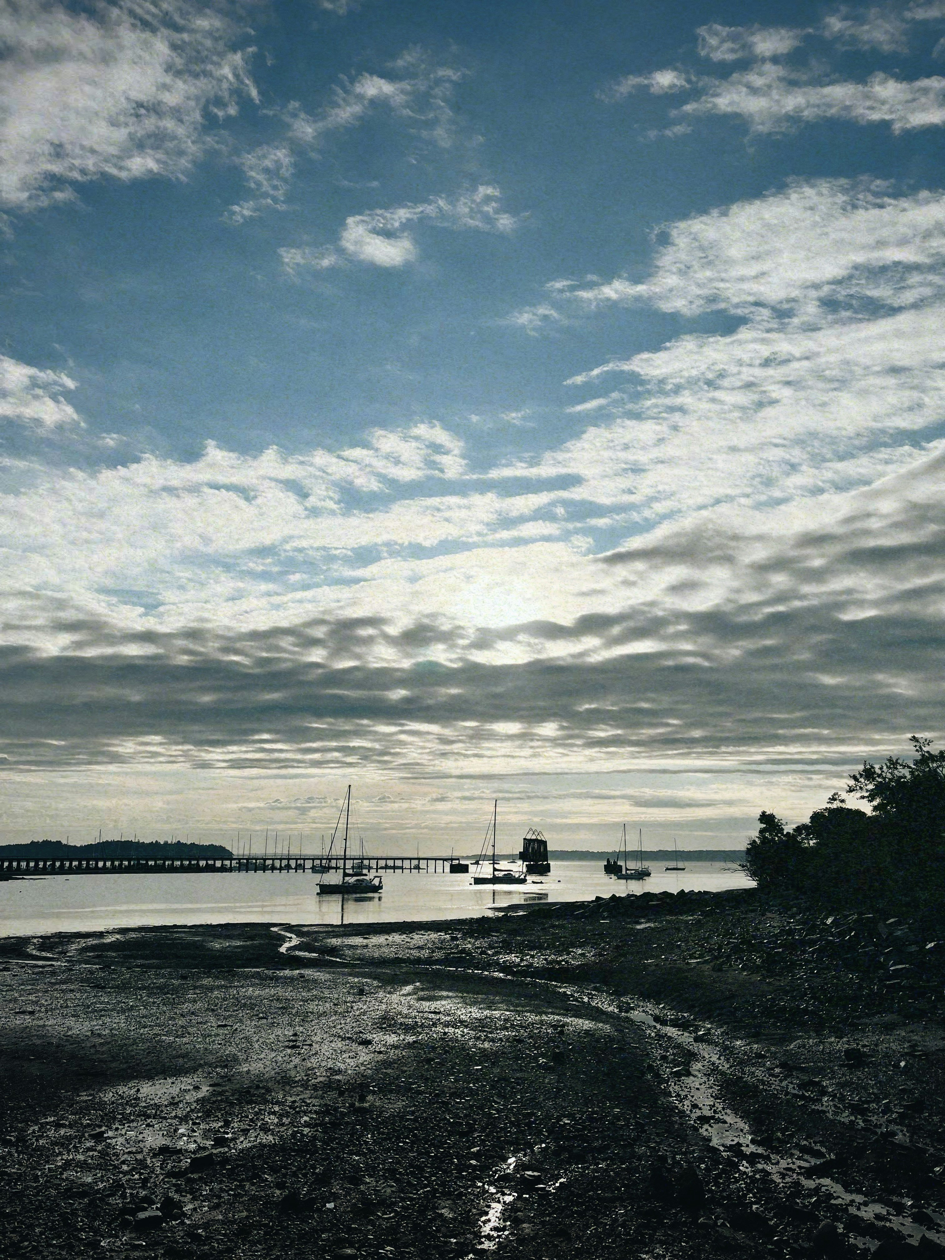 Sailboats anchored in a calm bay under cloudy sky.