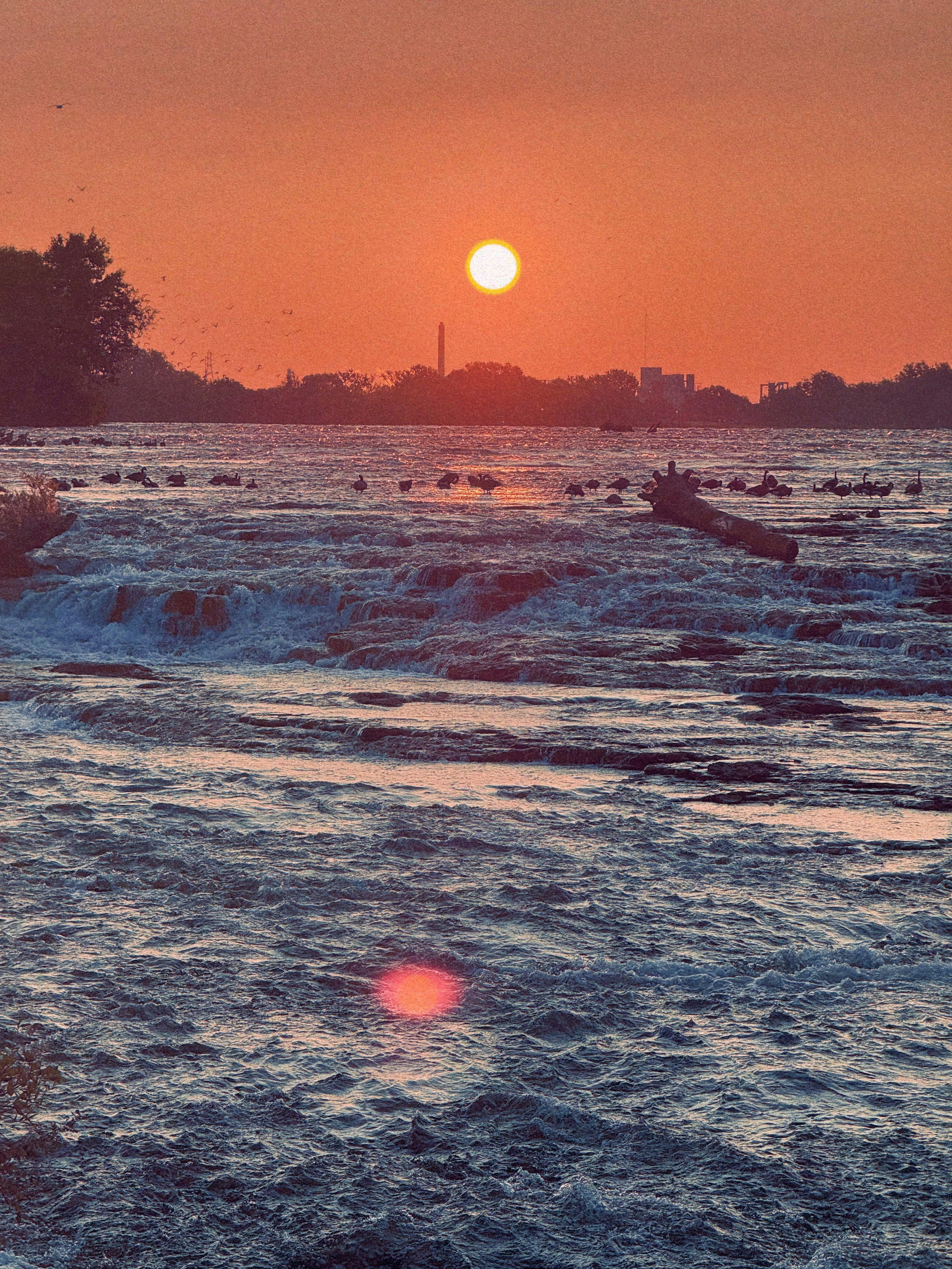 Sunset over a powerful river with distant cityscape.