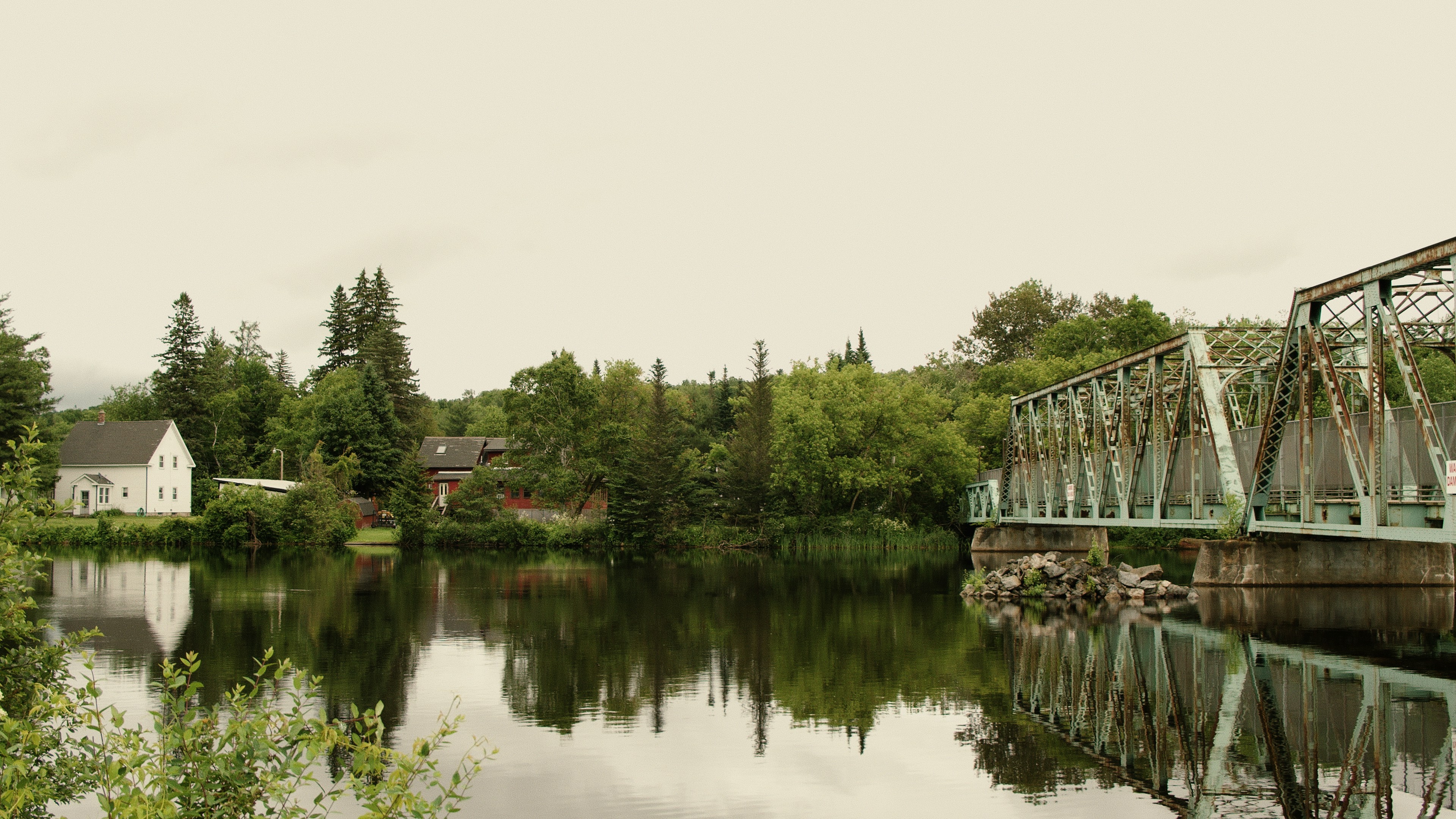 A bridge crosses a calm river near trees and houses.