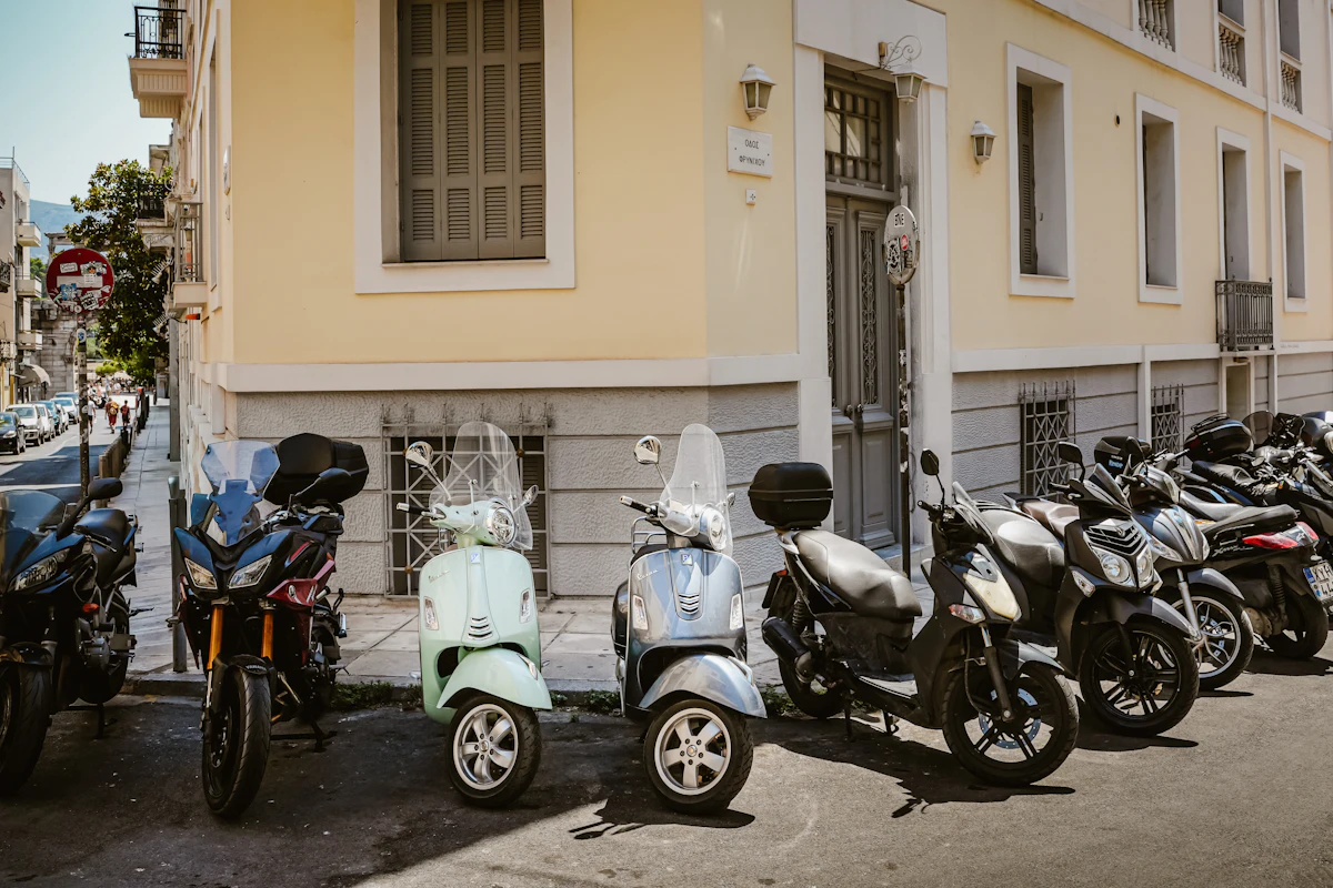 A row of scooters parked in hard midday sun against the ochre wall of an old town building.