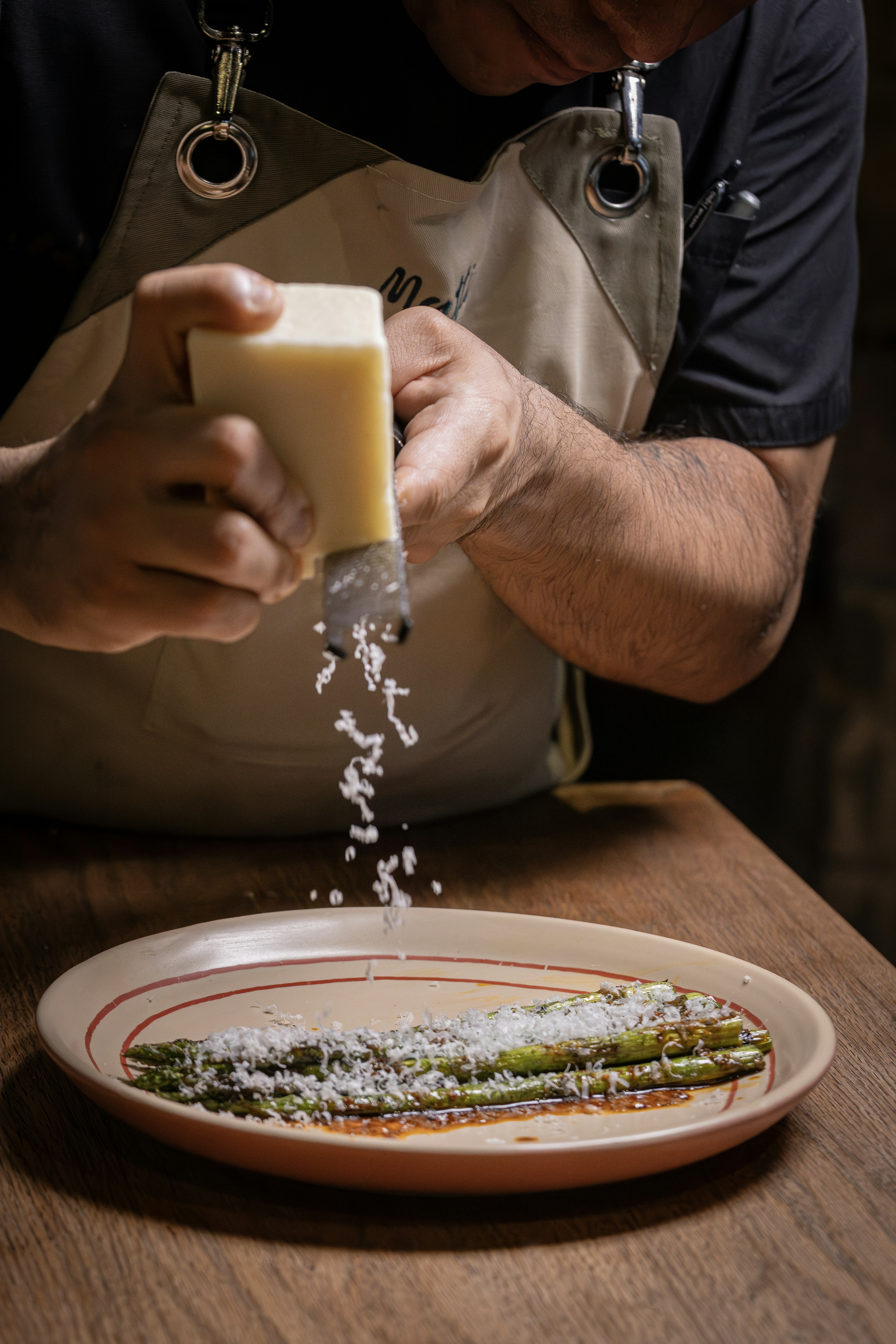 Chef grating cheese over grilled asparagus on a plate