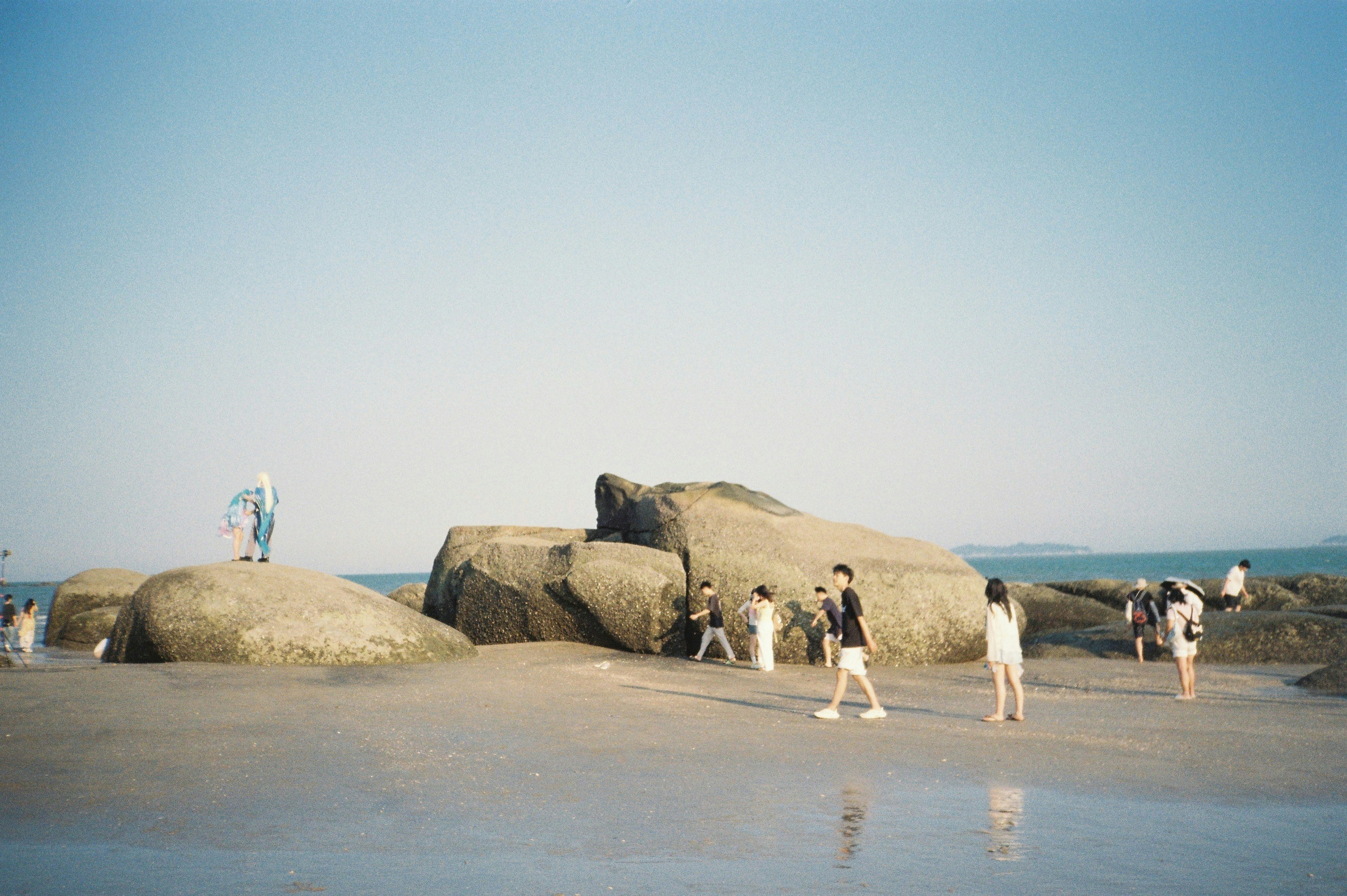 People exploring a rocky beach with calm ocean water
