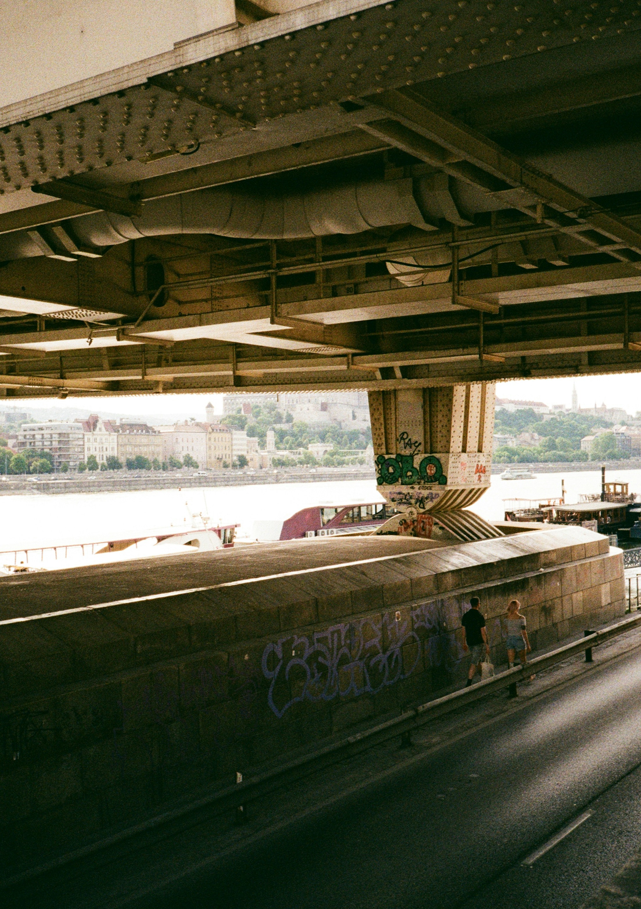 People walk beneath a large concrete bridge over a river