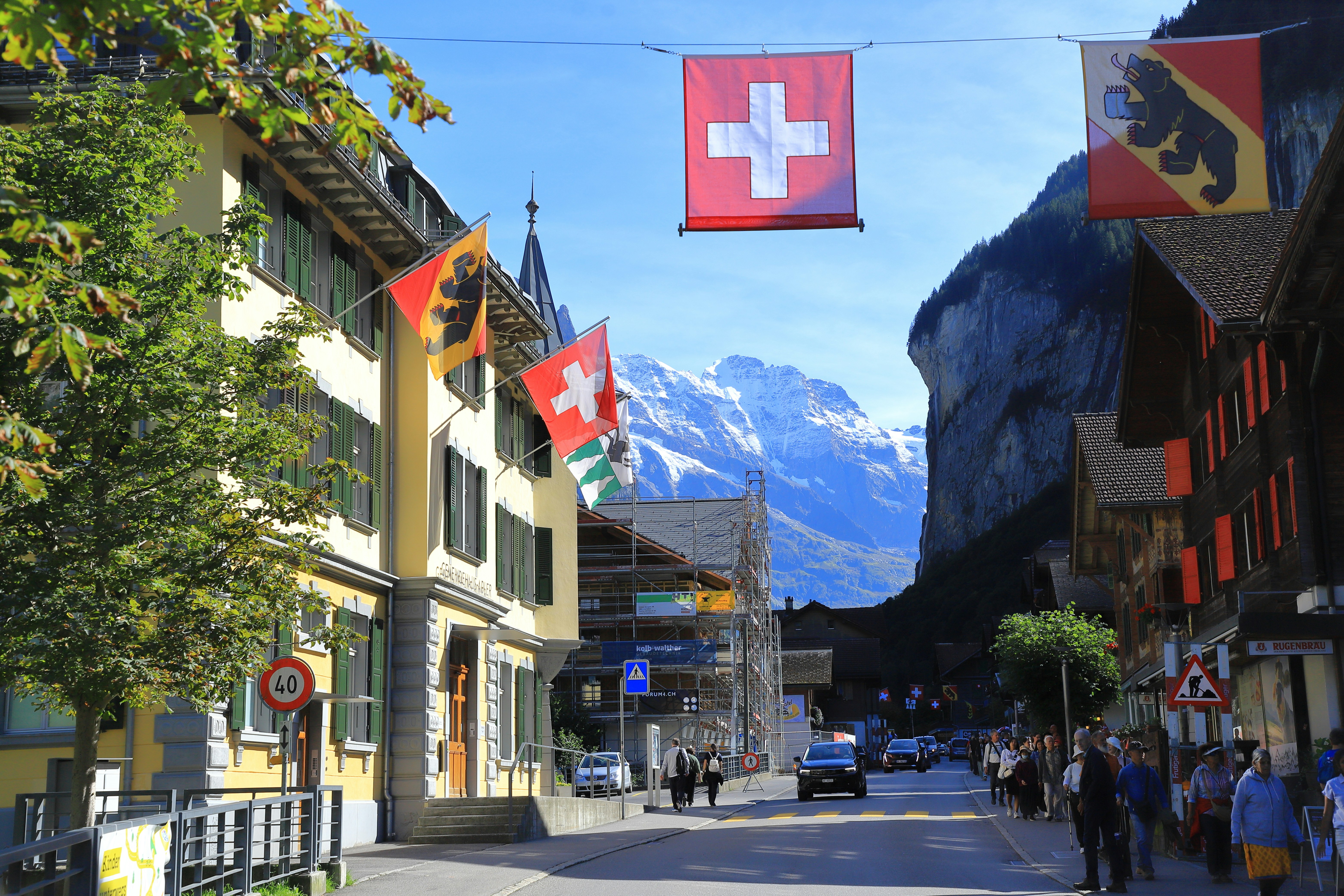 Swiss flags hang over a street with mountains behind.