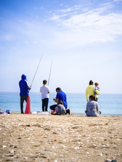 People fishing on a sunny beach by the ocean.