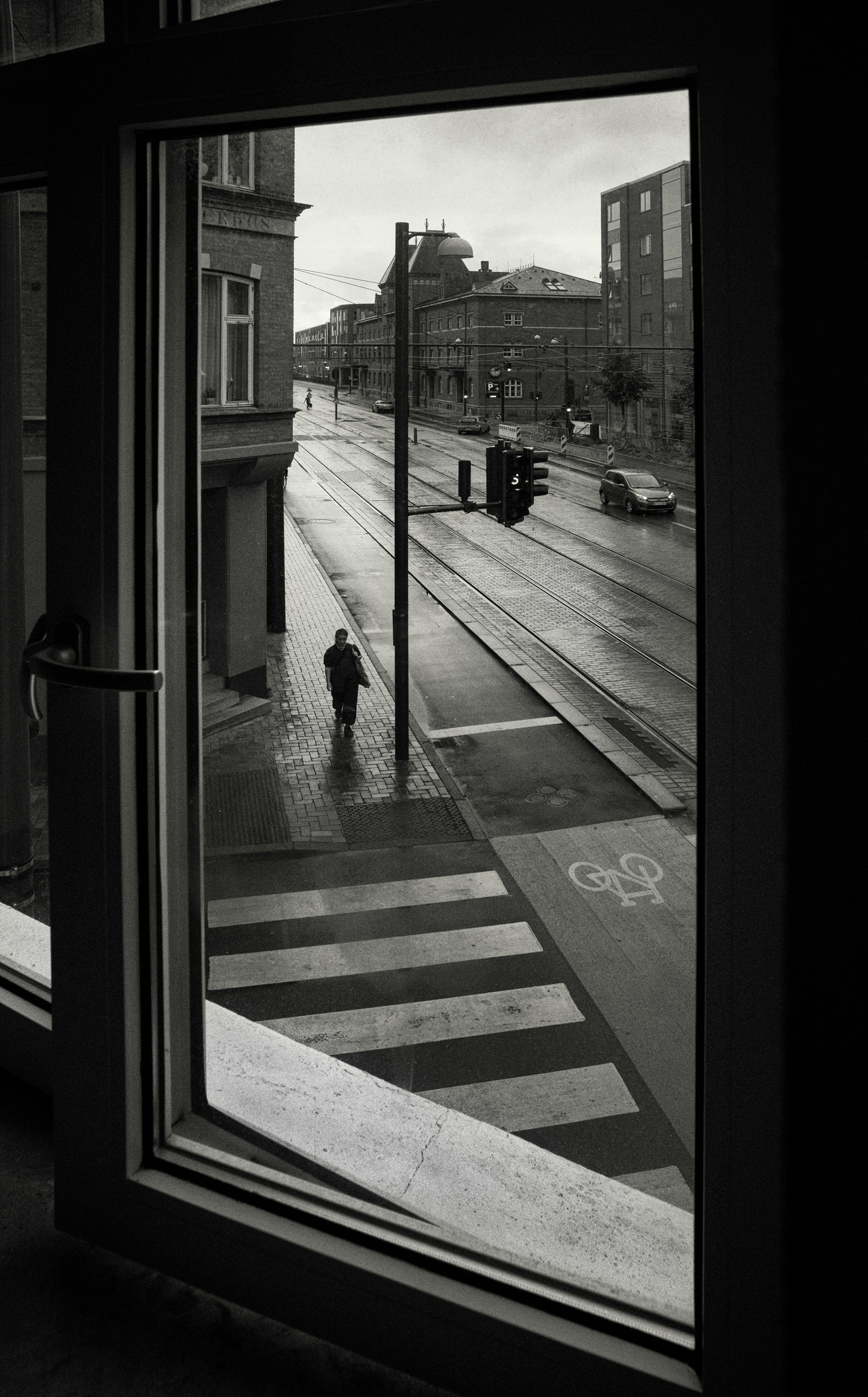 Person walks across wet street through open window