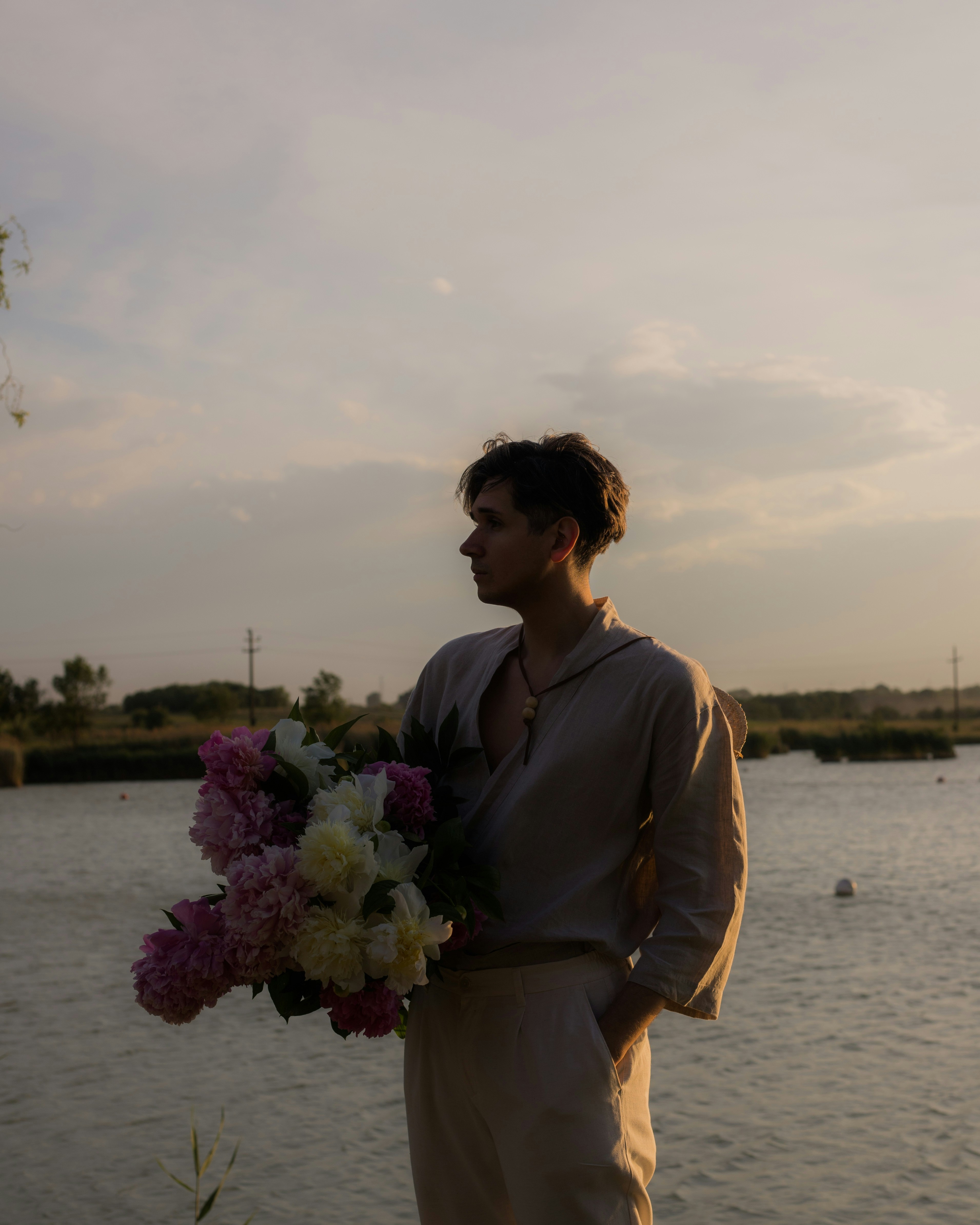Uomo che tiene un mazzo di peonie vicino all'acqua