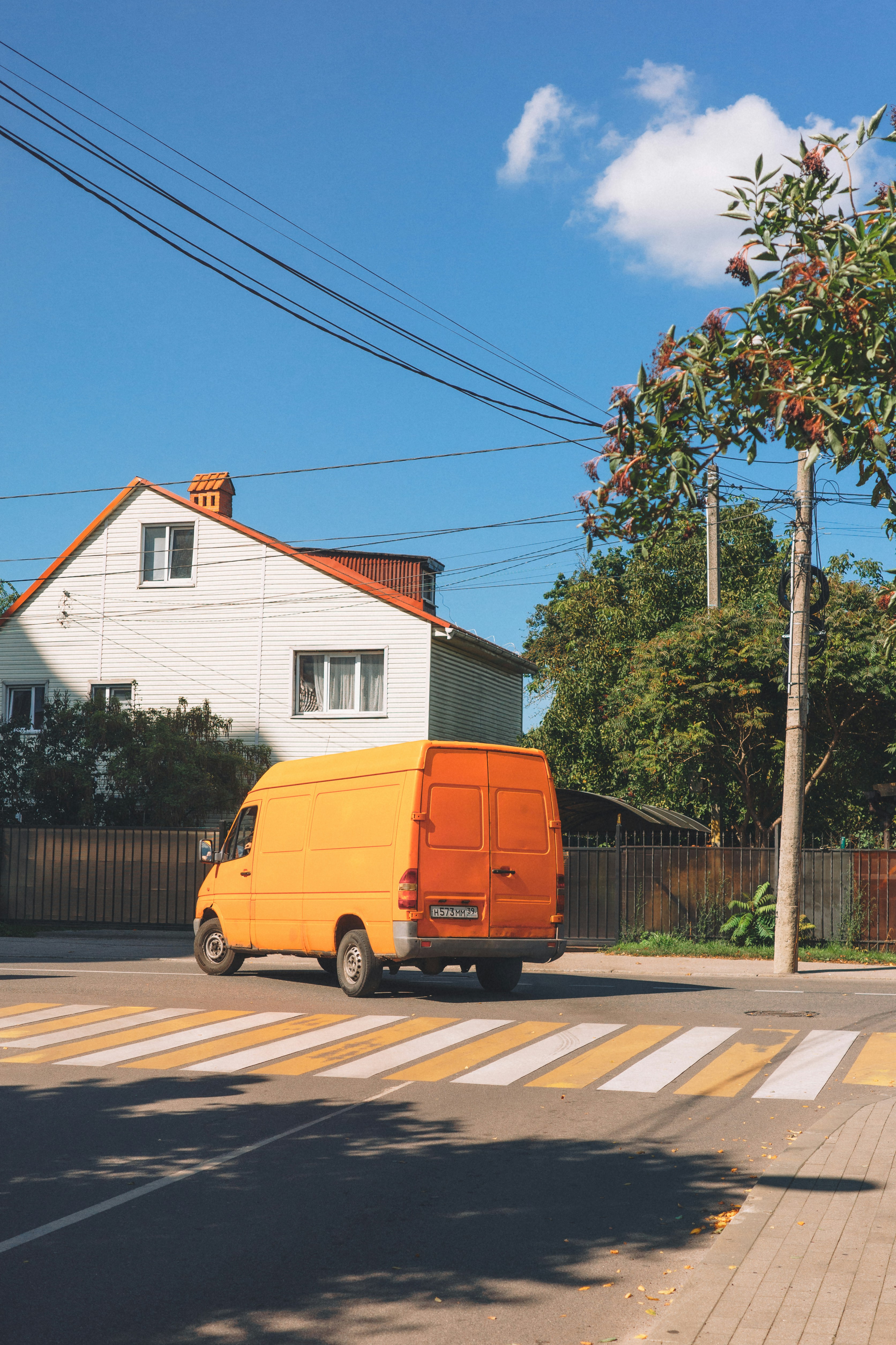 Orange van drives across a crosswalk near a house.