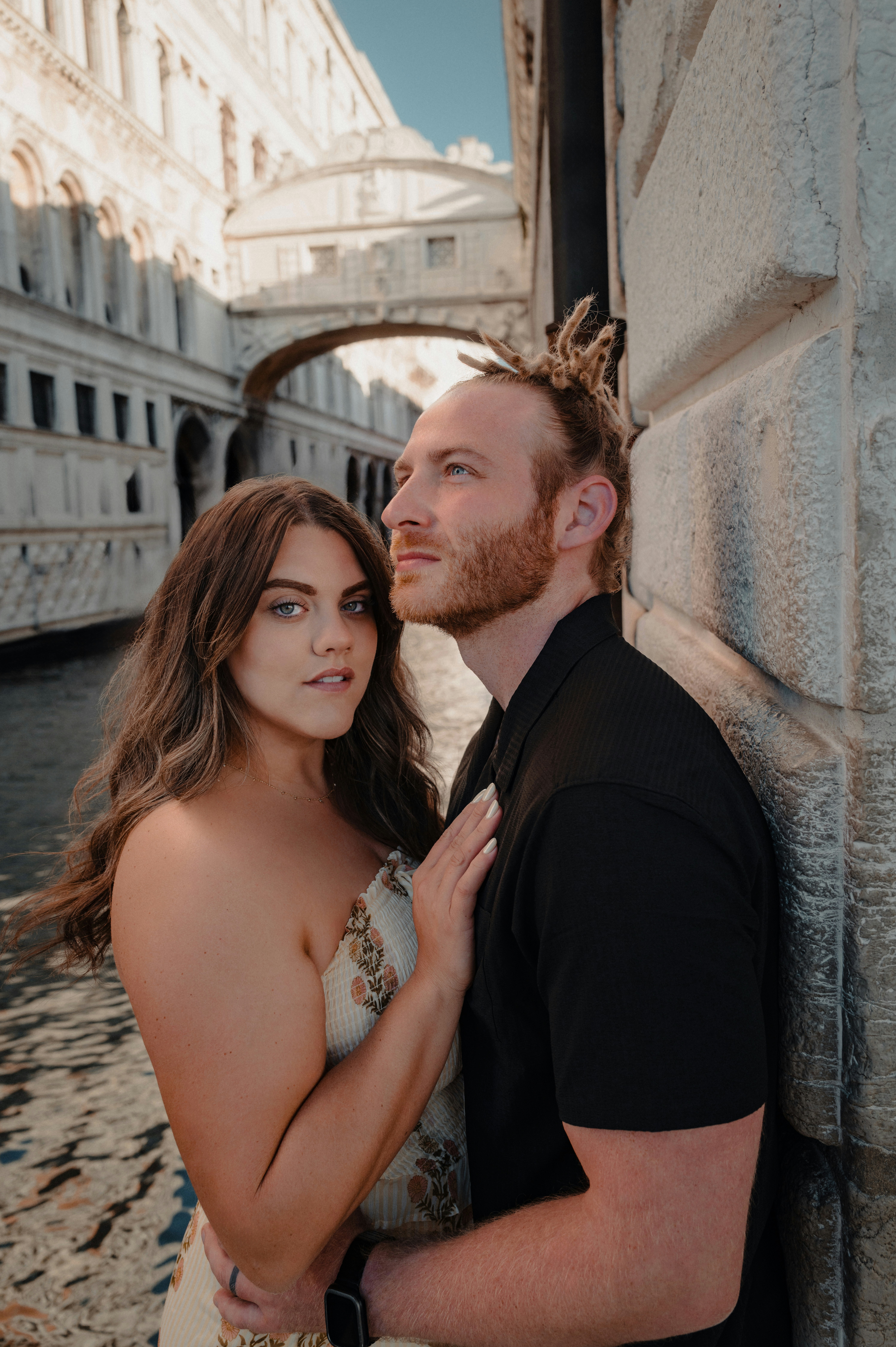 Casal posando por um canal com uma ponte atrás deles.