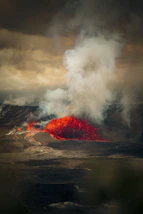 Molten lava erupting from a volcano under cloudy skies.