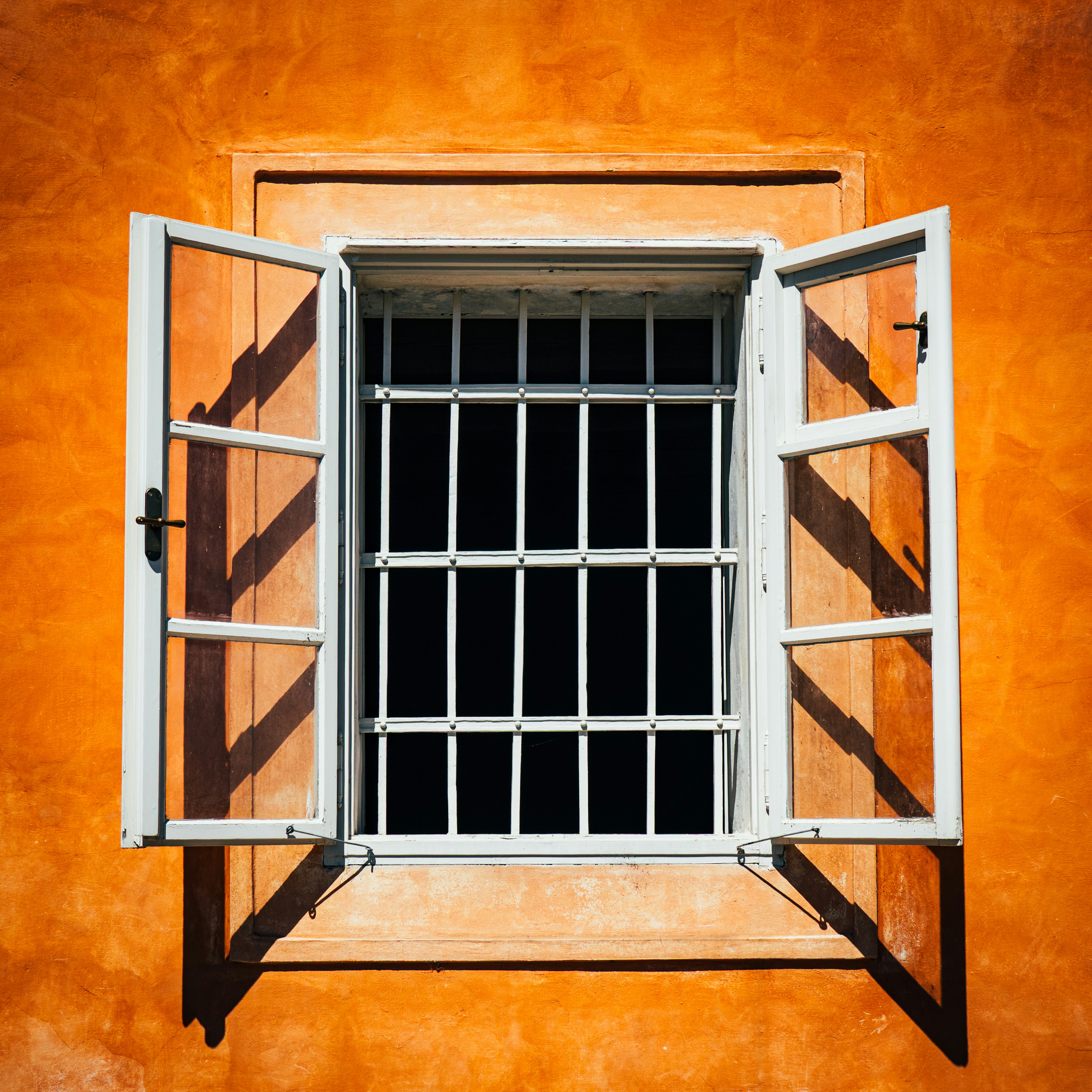 Offenes Fenster mit weißen Gittern an orangefarbener Wand.