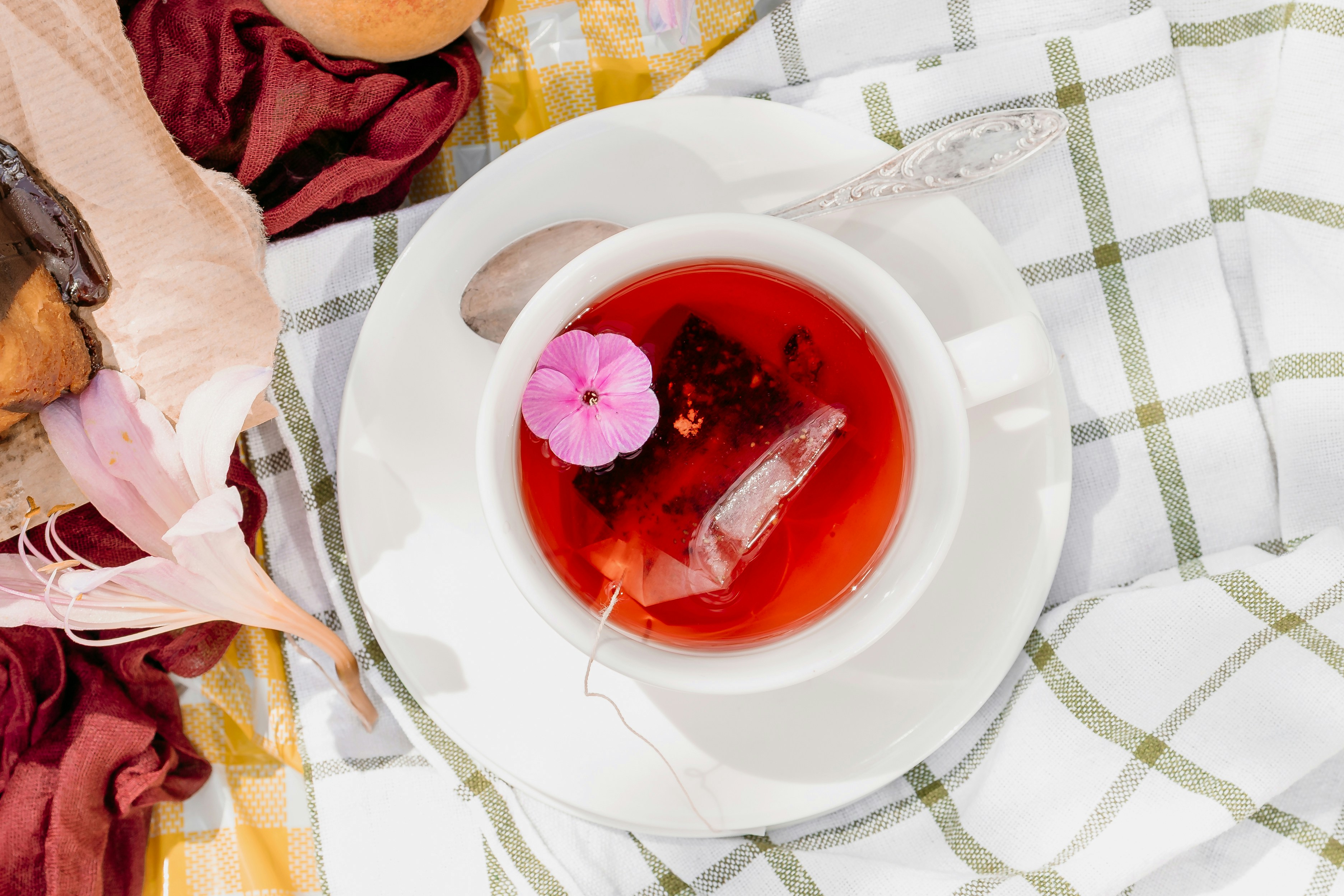 A cup of red tea with a flower and tea bag.