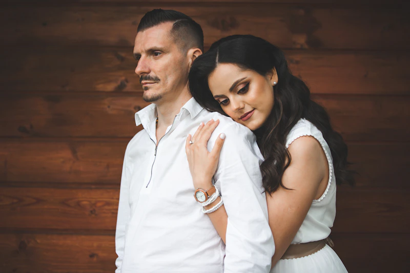 couple in white clothing embracing by a wooden wall