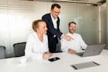 Three colleagues collaborating around a laptop in a meeting room.