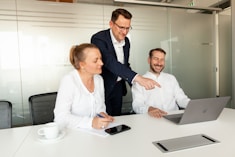 Three colleagues collaborating around a laptop in a meeting room.
