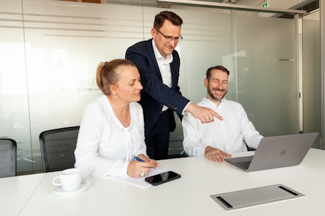 Three colleagues collaborating around a laptop in a meeting room.