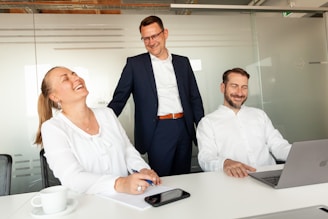 Three colleagues laughing together in an office setting.
