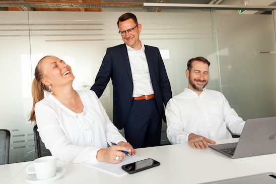 Three colleagues laughing together in an office setting.