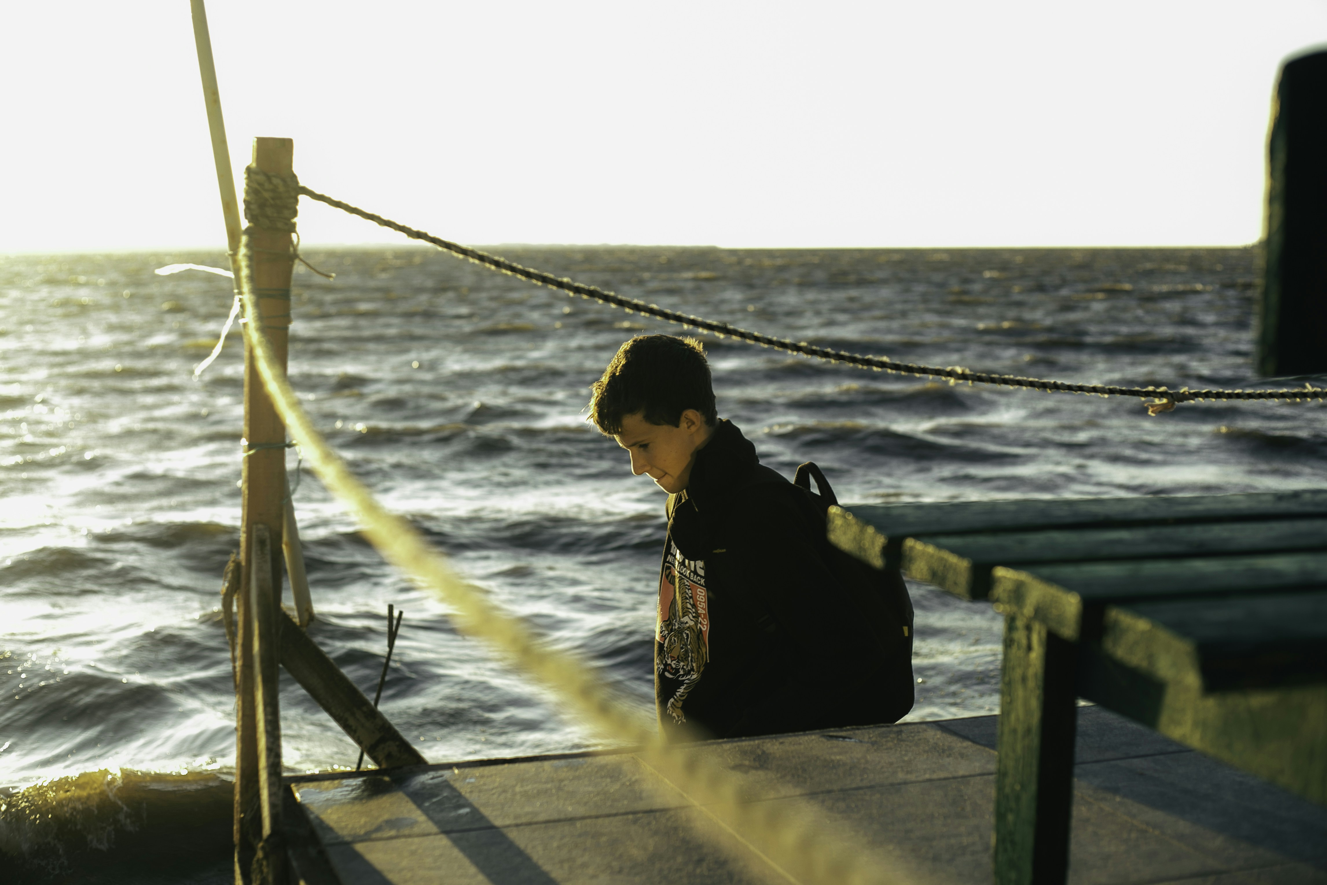 Giovane ragazzo con zaino si siede in riva all'oceano.