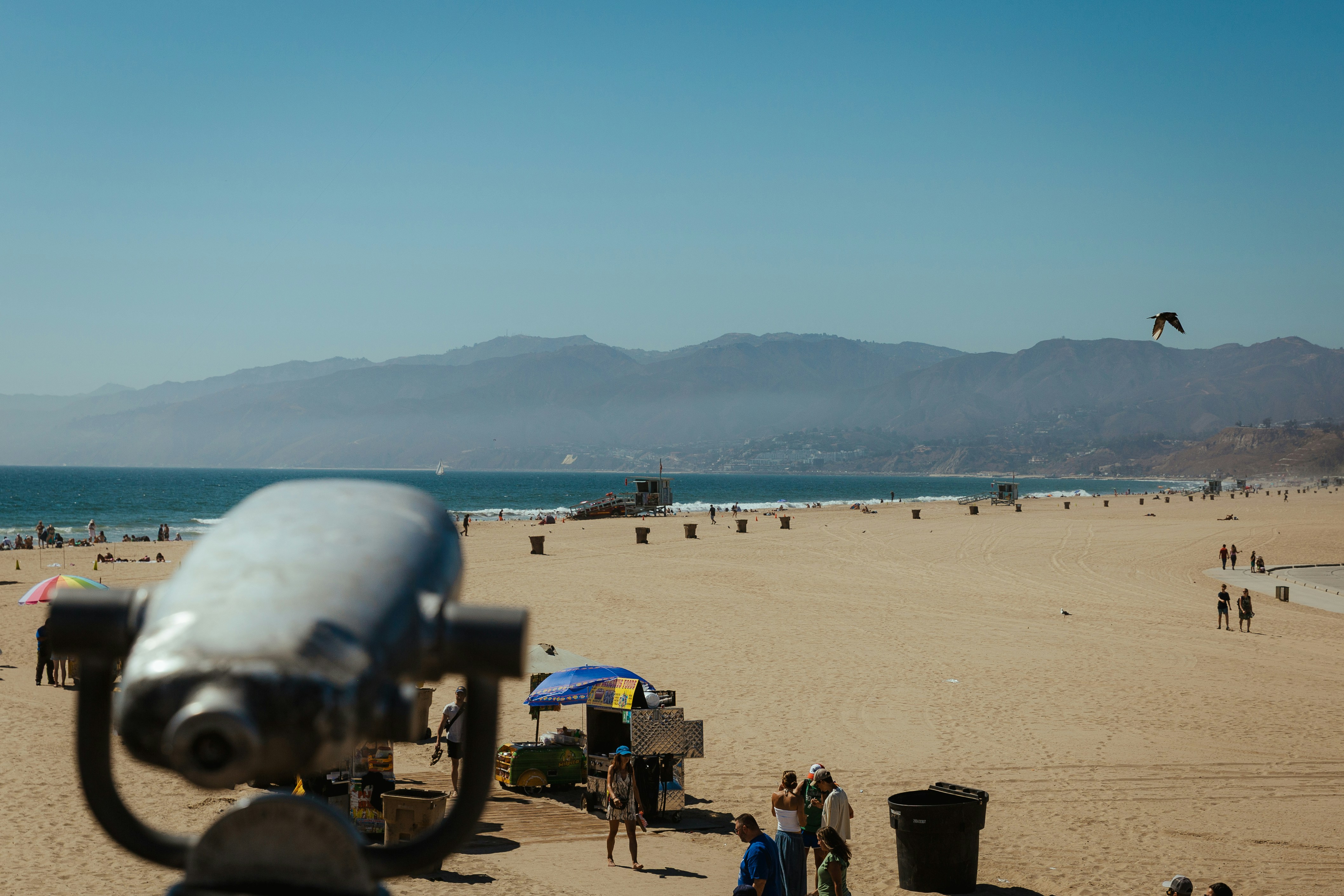 Binoculars overlook a busy beach with distant mountains.