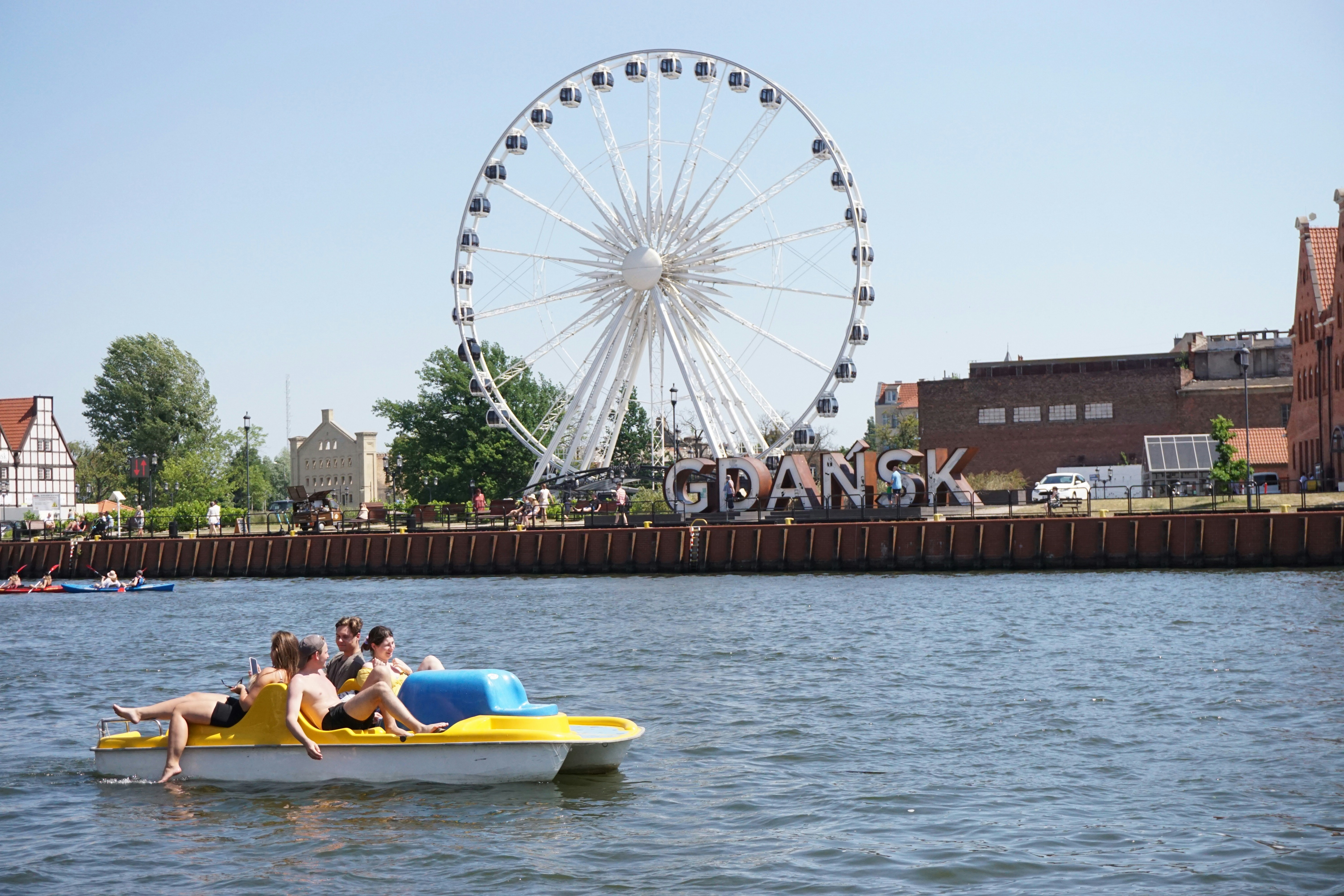 Menschen auf einem Tretboot mit Riesenrad und Stadt im Hintergrund