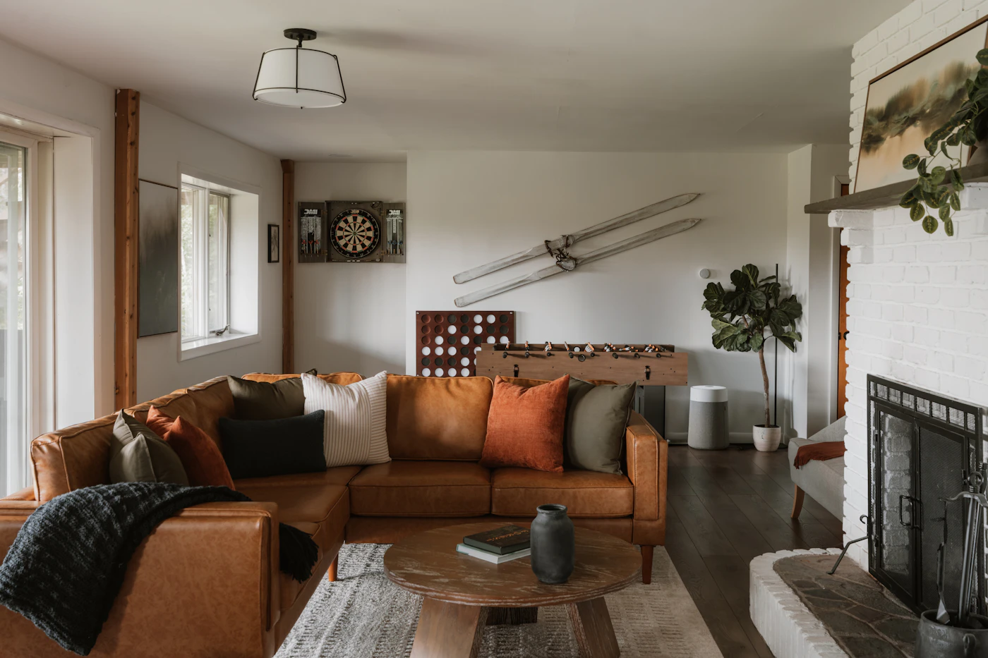A cozy living room with a brown sectional sofa, green houseplants, warm lighting and a fireplace