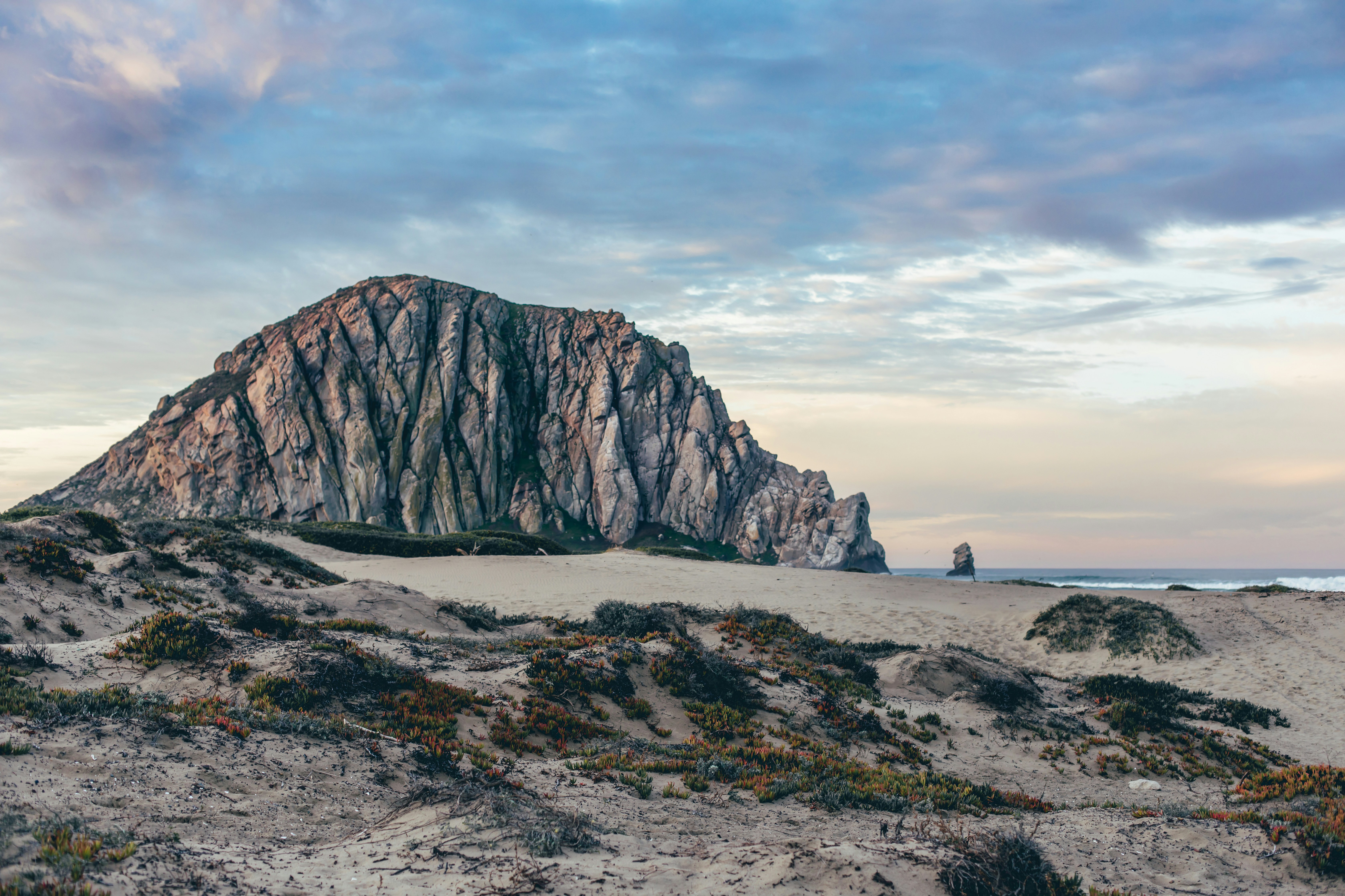 Large rock formation on a sandy beach at sunset.