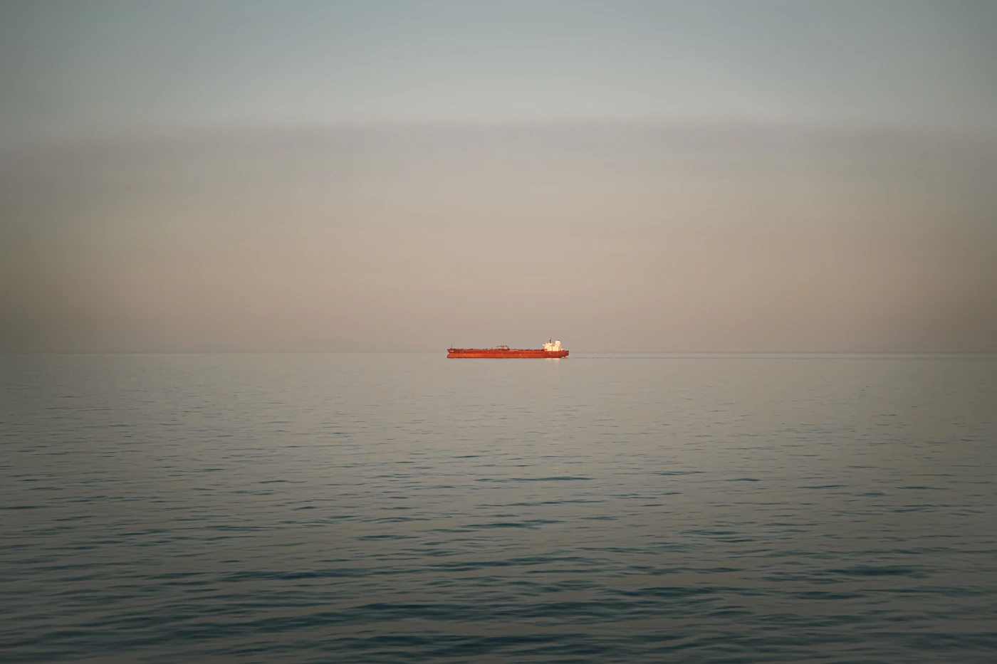 A lone ship on a vast, calm ocean at dusk with the horizon fading, representing waters far beyond the three nautical mile line
