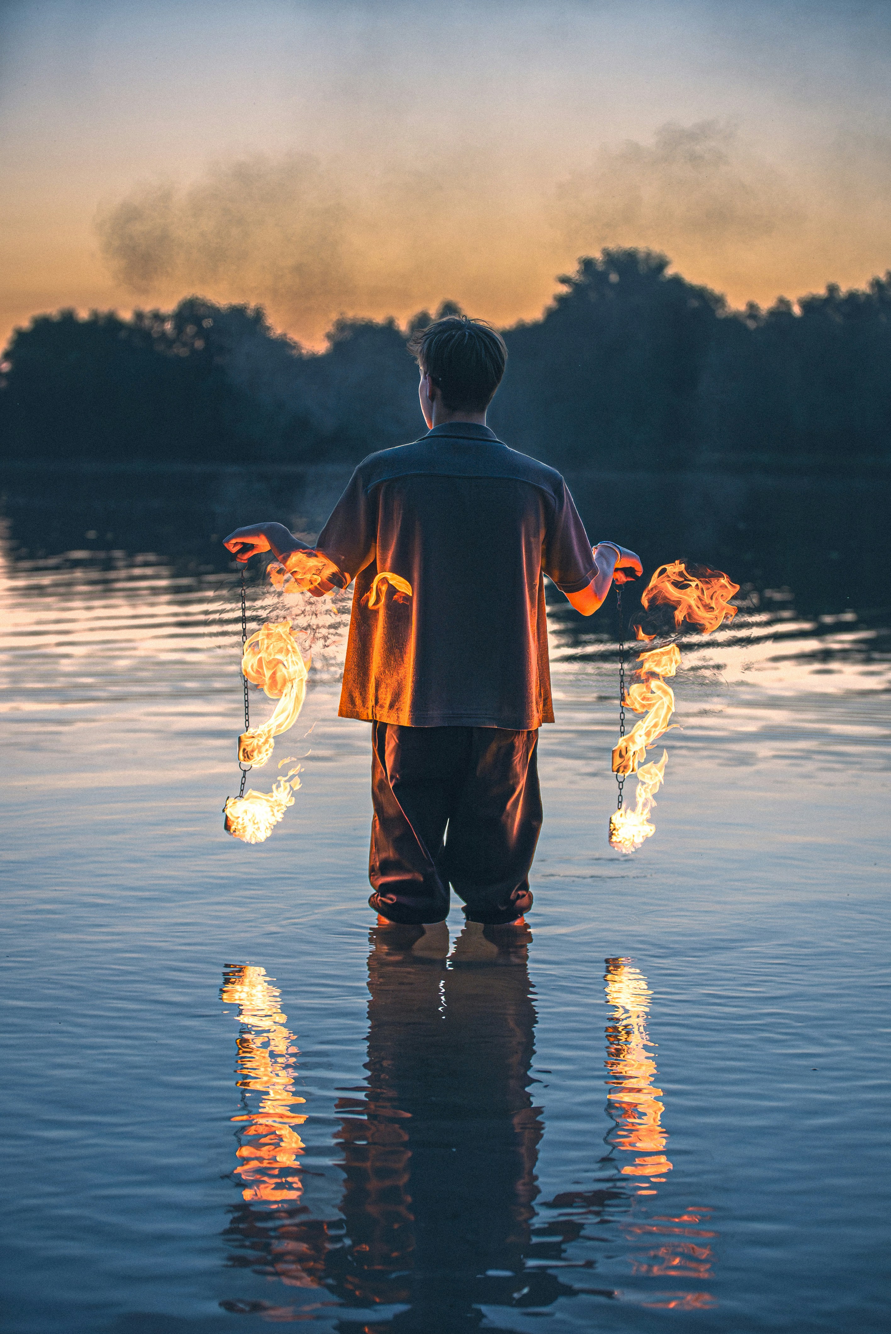 Man standing in water holding burning torches at sunset
