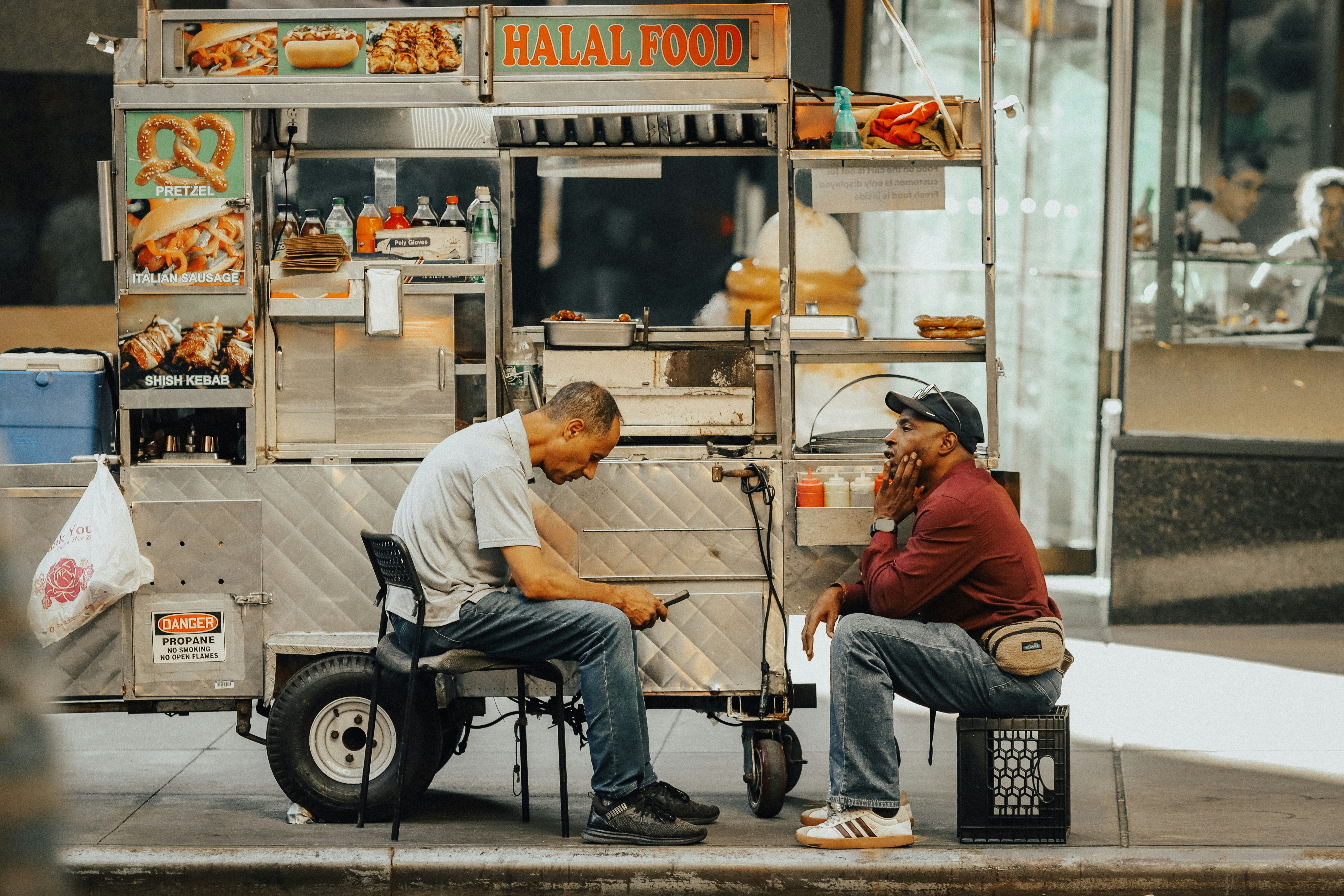 Two men sitting by a halal food cart.