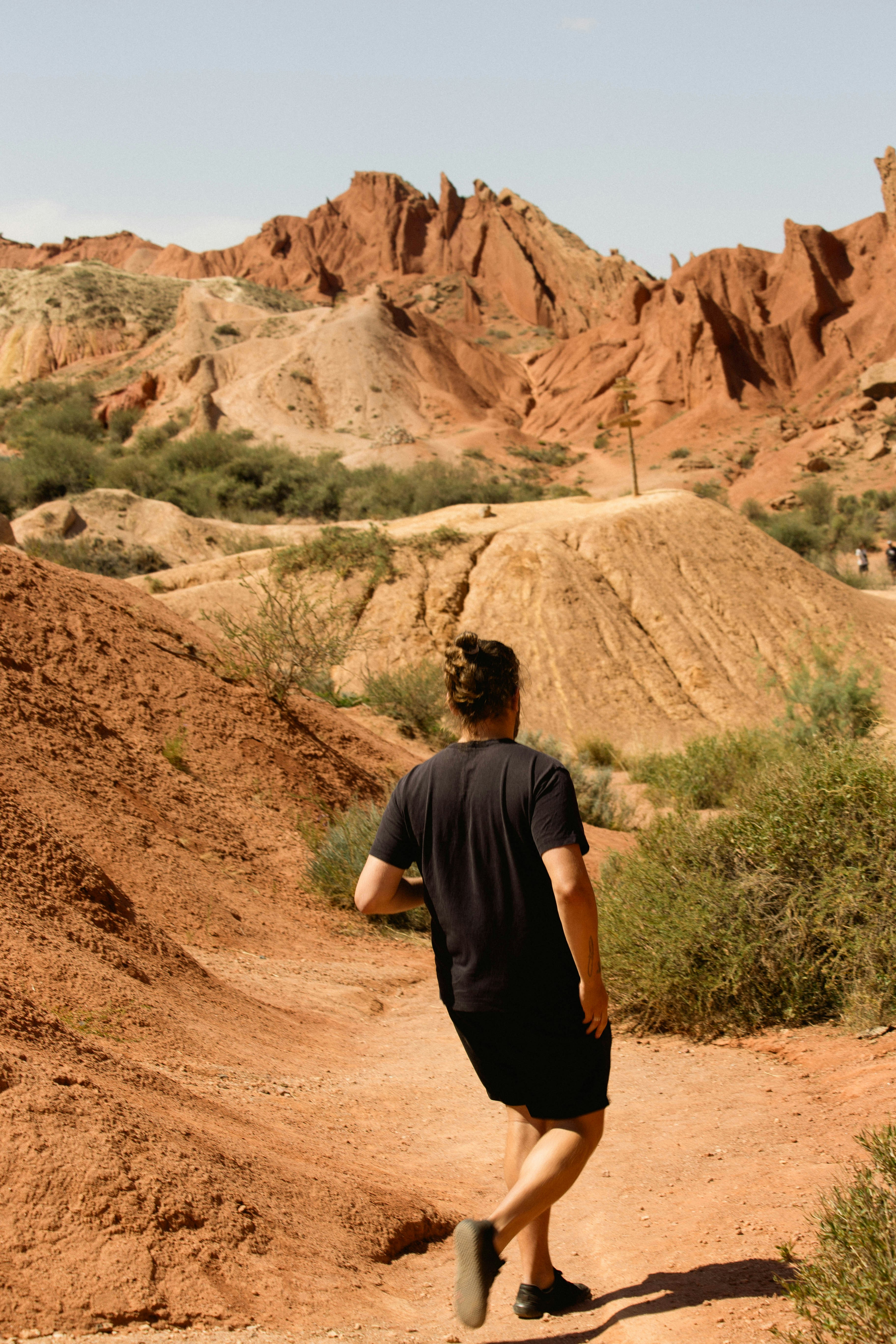 Man walking through a desert canyon with red rock formations.