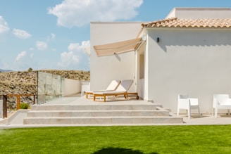 Modern white villa with lounge chairs and green lawn.