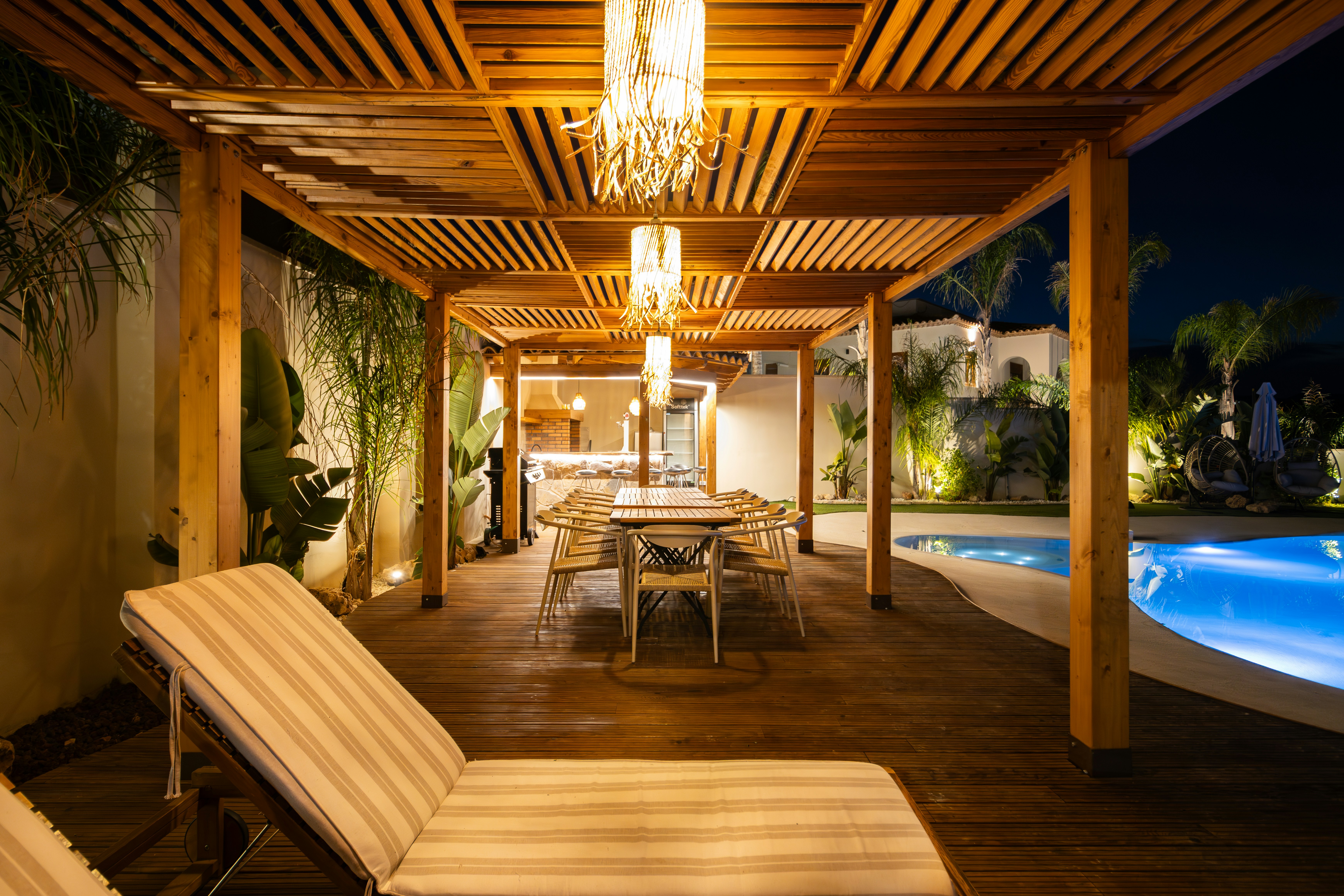 Outdoor dining area with lounge chairs and pool at night