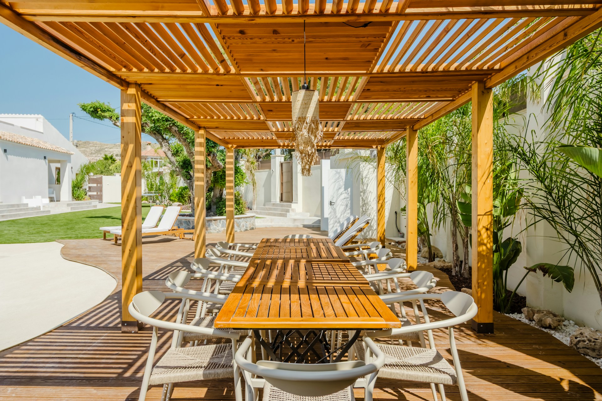 Wooden pergola with dining table and chairs outdoors.