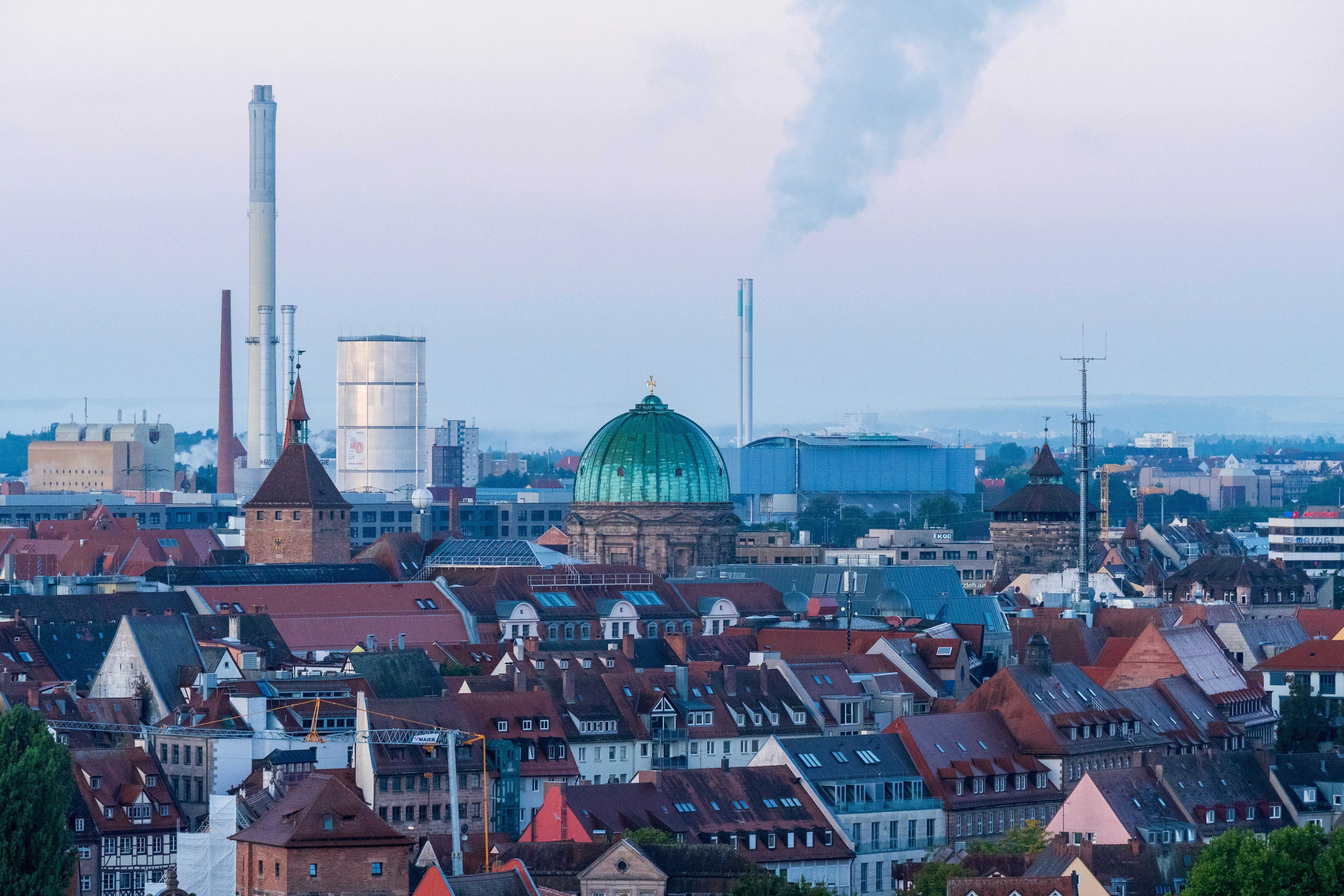 Cityscape with industrial smokestacks and a green dome.