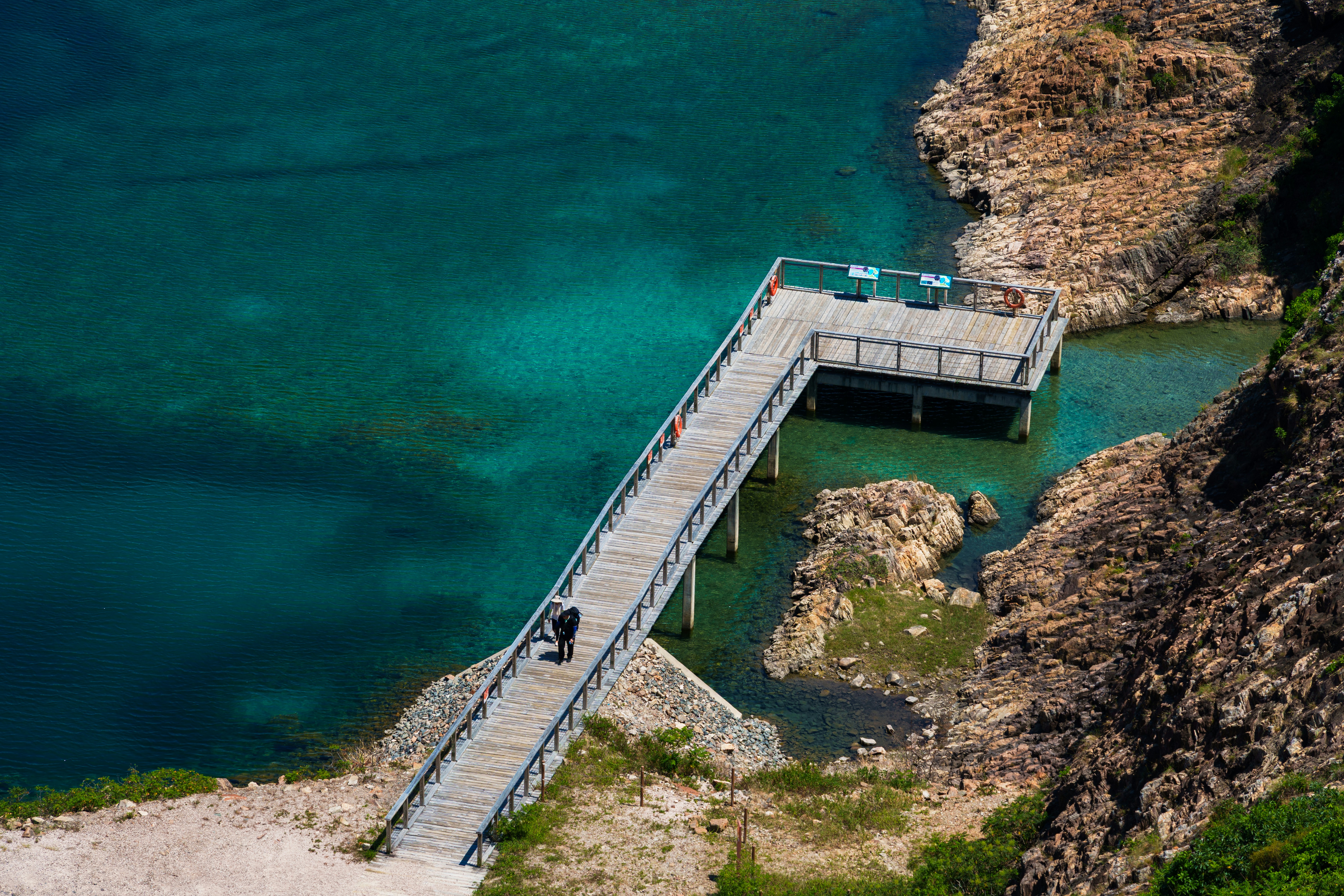 Wooden walkway over clear blue water near rocky shore