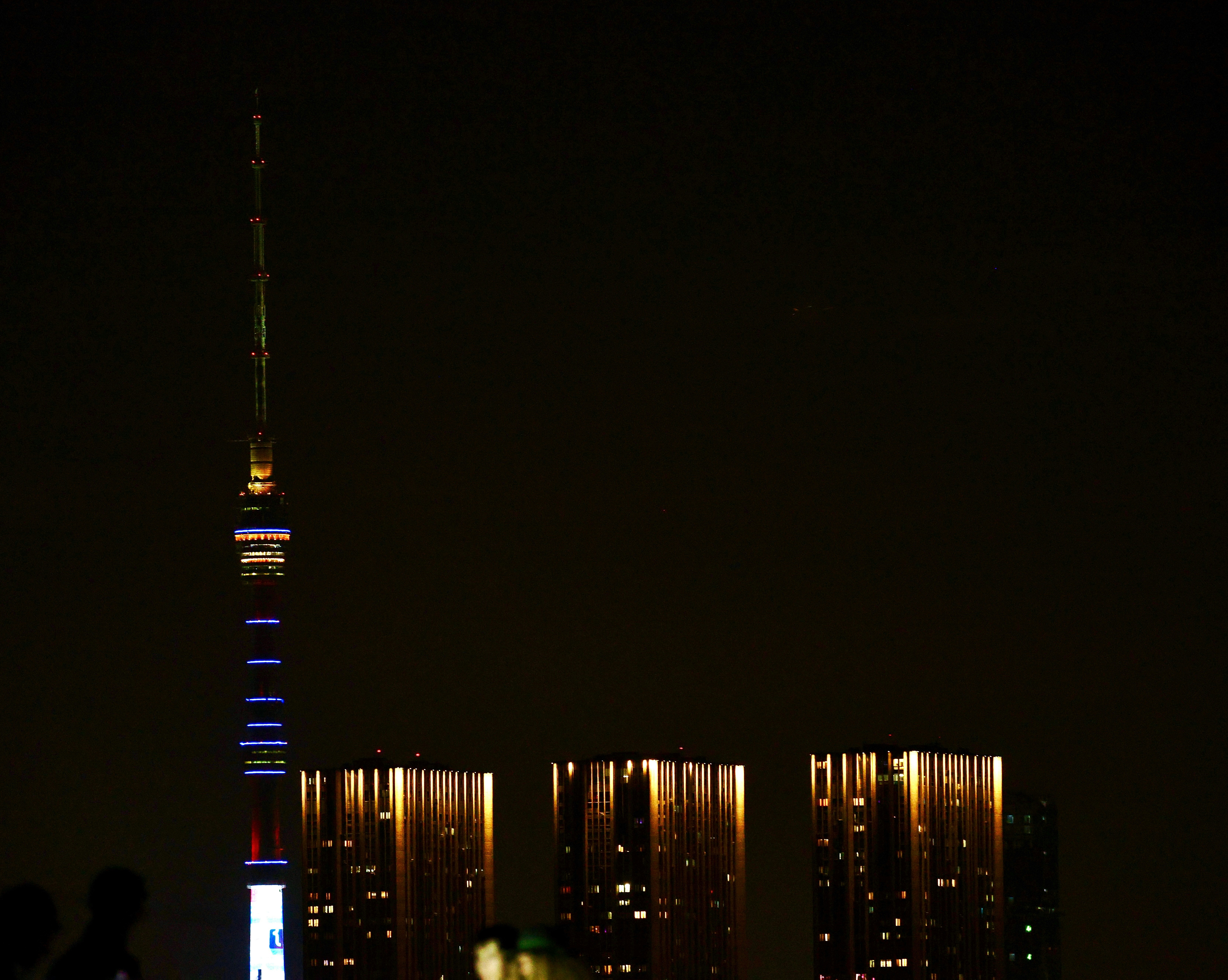 Tall illuminated tower with city buildings at night