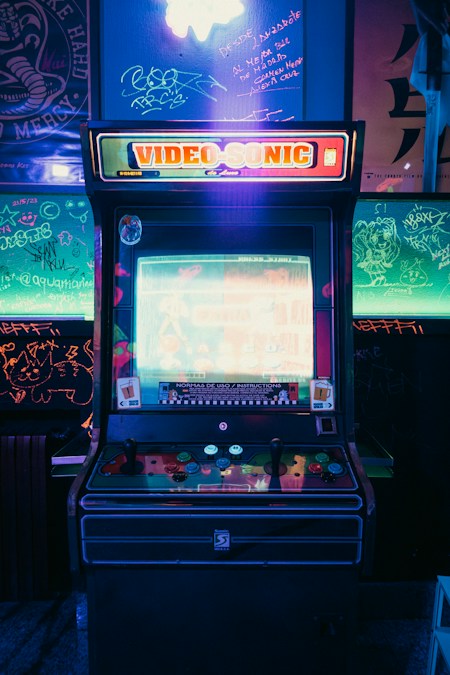 Une borne d’arcade rétro affichant un jeu de combat, entourée de murs couverts de graffitis éclairés au néon vert (photo d’illustration)